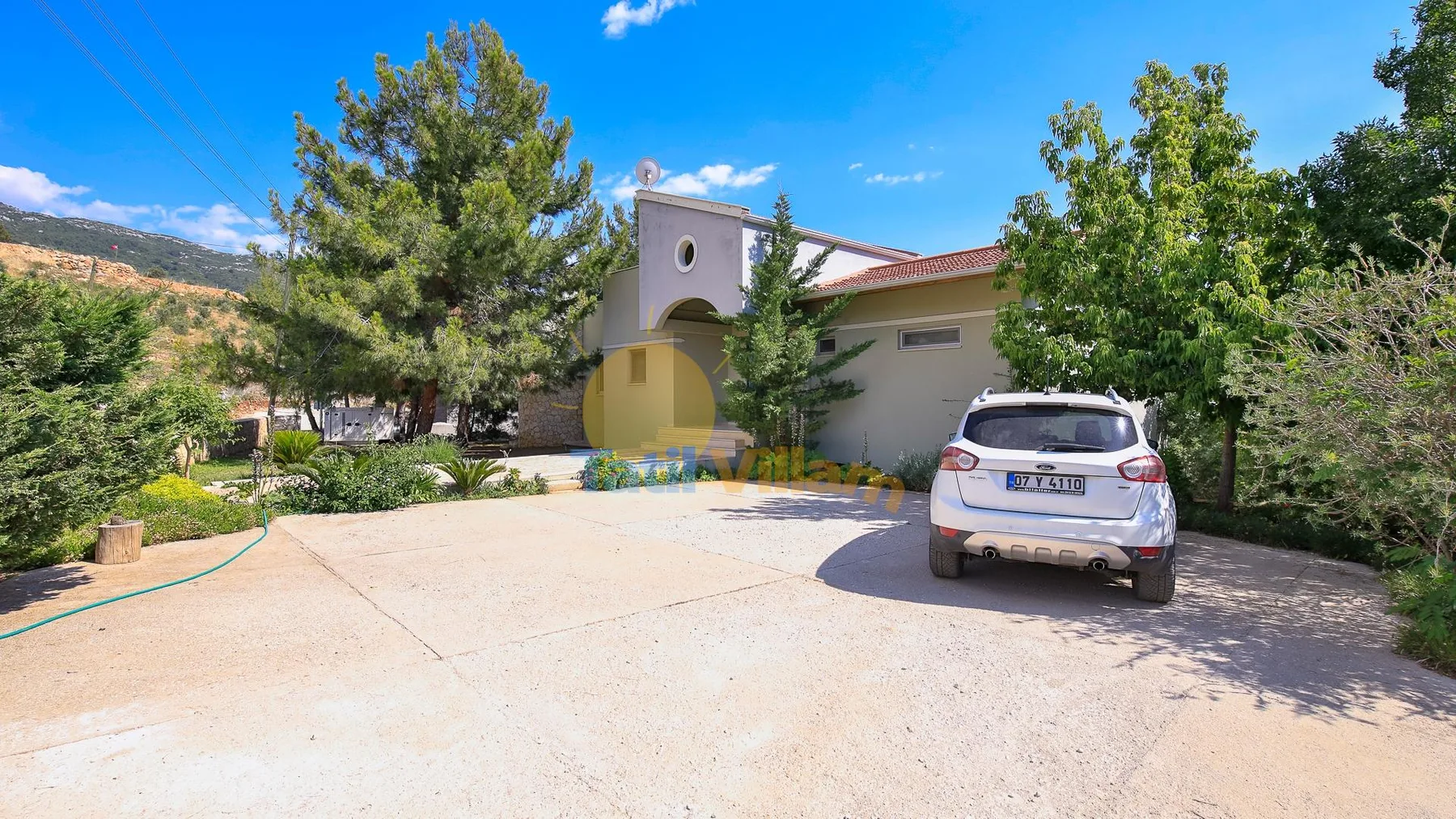 A house stands beside a broad paved driveway, with a car parked in front.