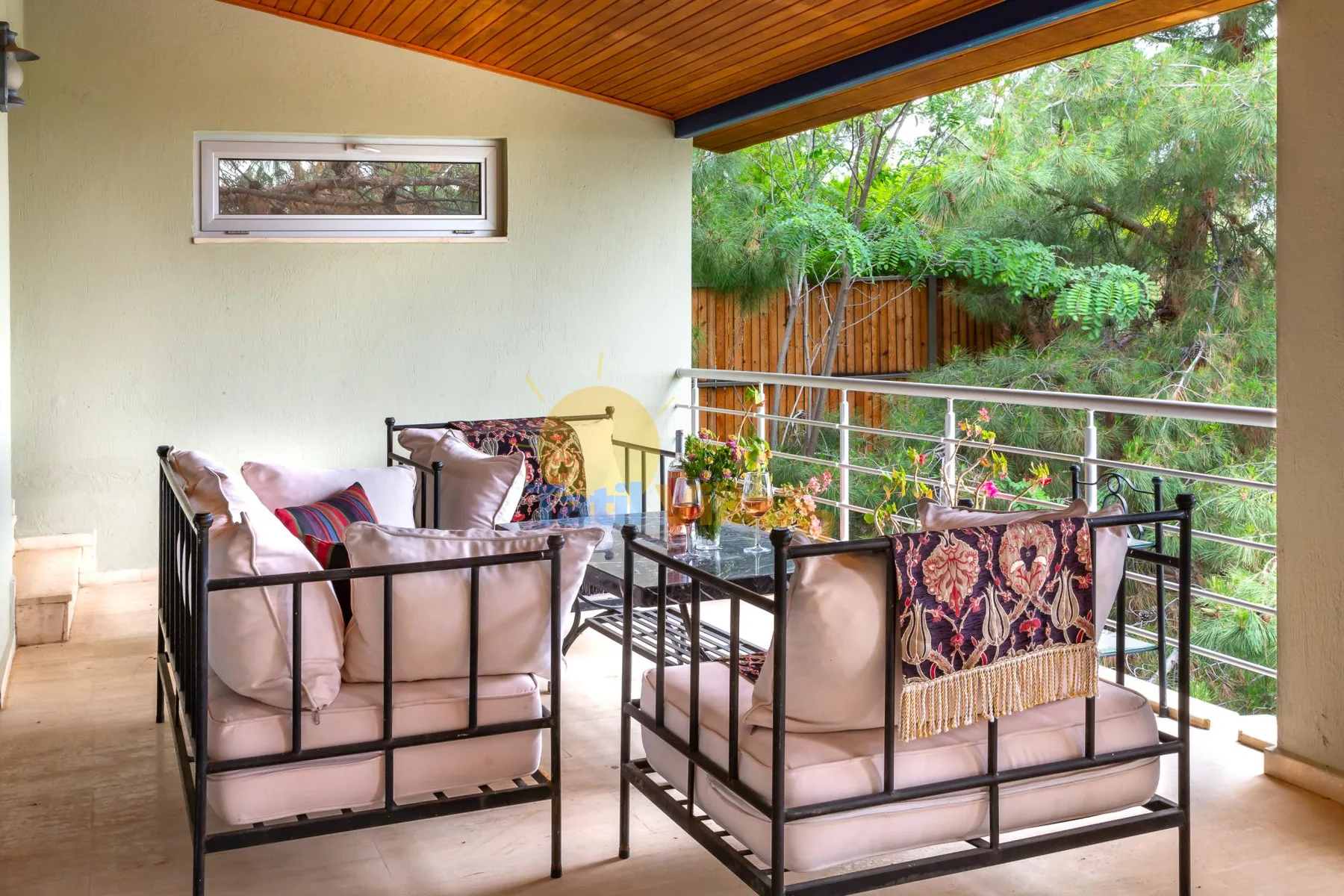 A covered outdoor seating area with cushioned seats and a garden view.