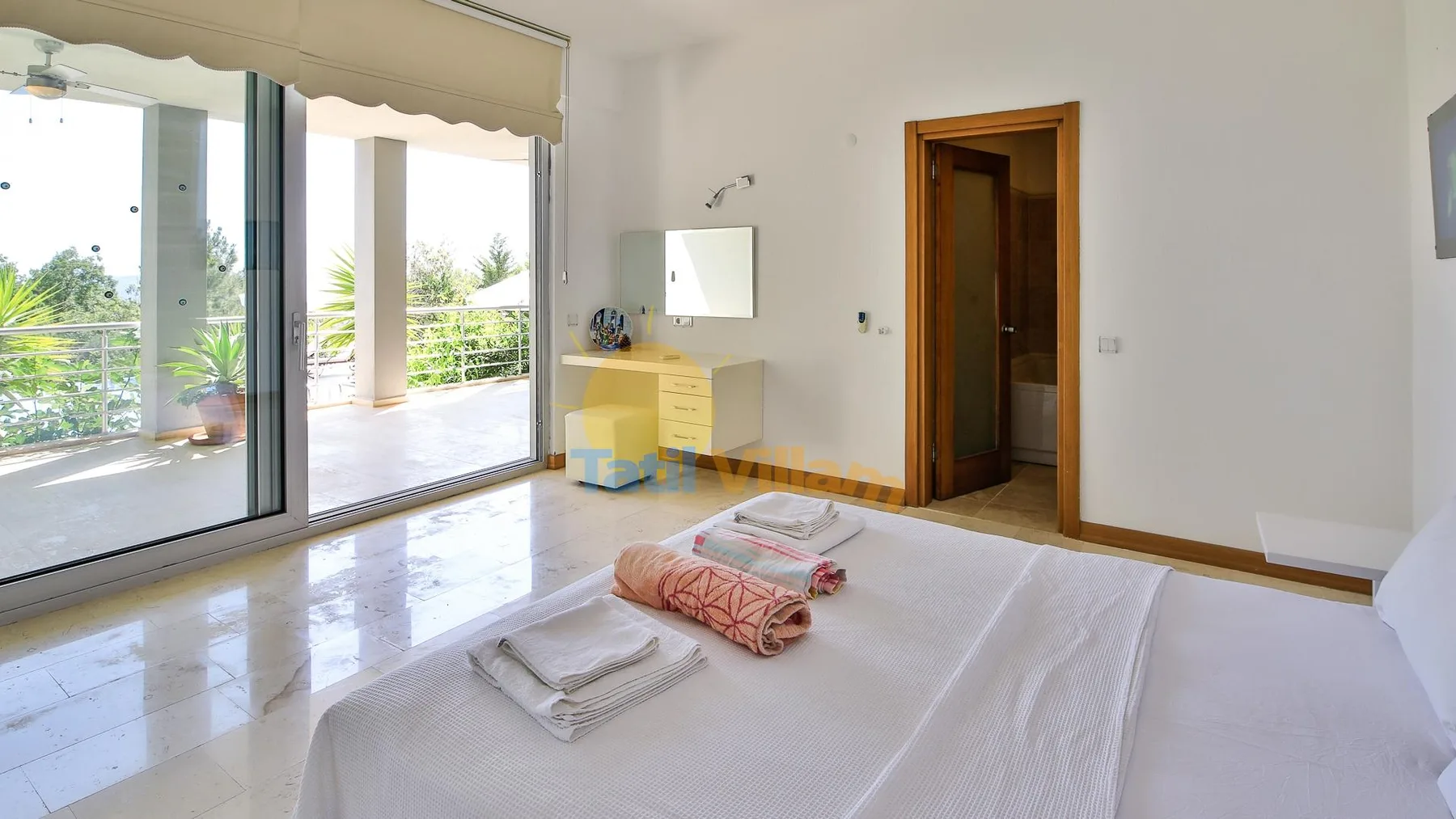 A bedroom with a neatly made bed beside wide glass doors opening onto a terrace.
