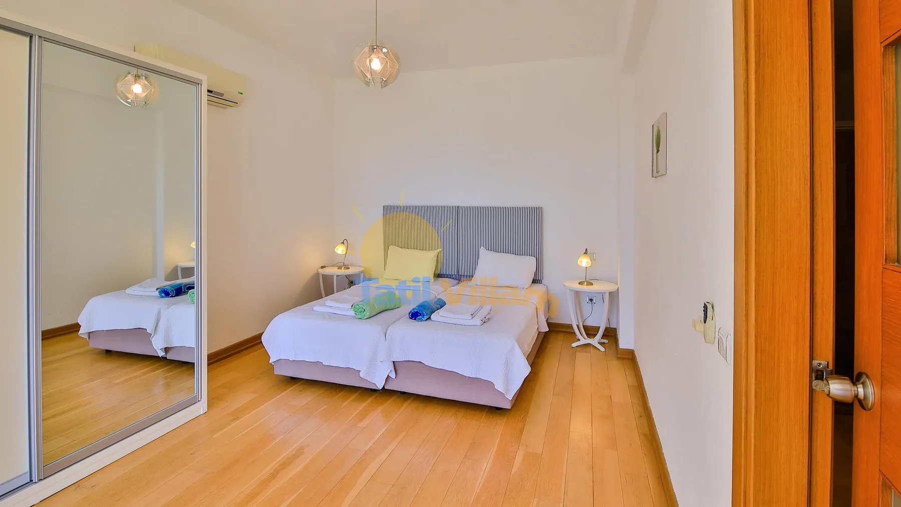 A bright bedroom with two beds and mirrored wardrobe doors.