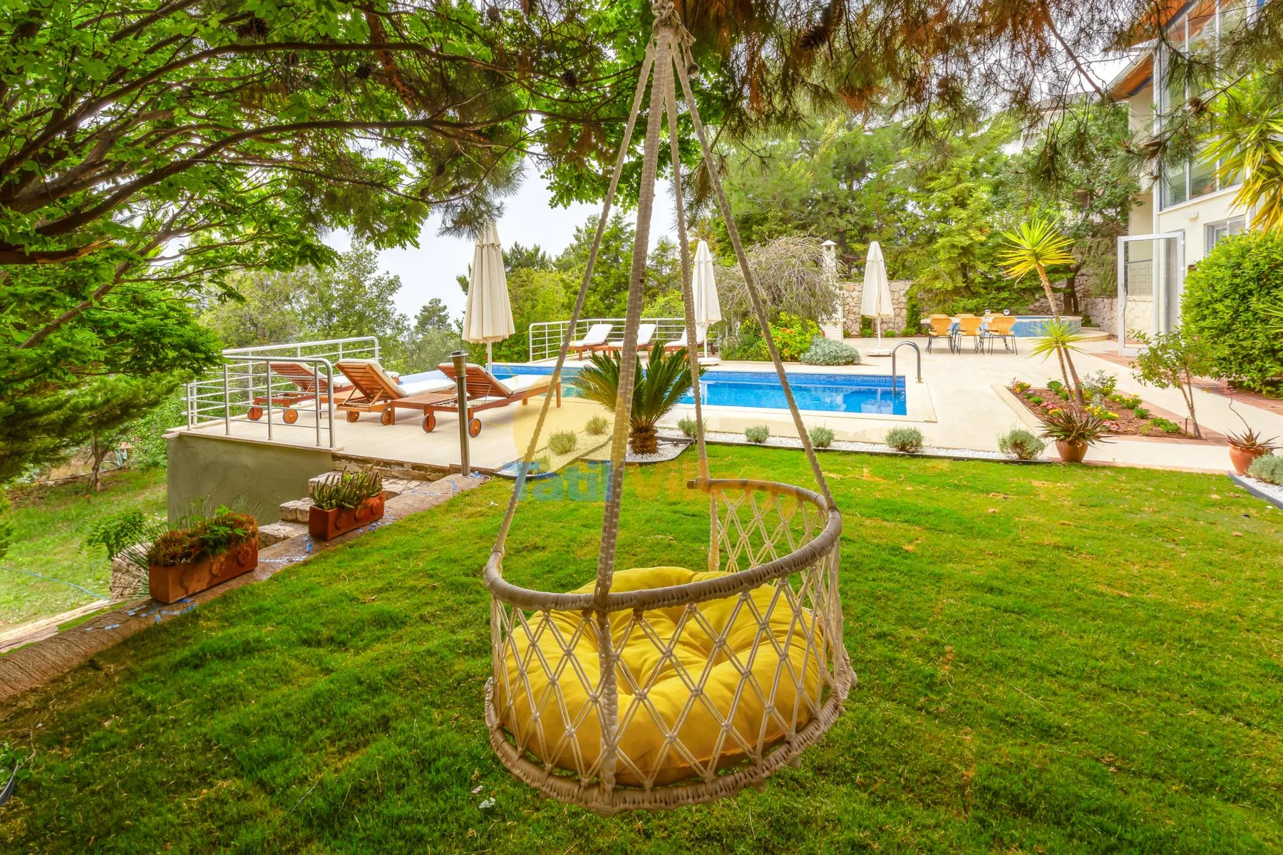 A landscaped outdoor pool area with lounge seating and a hanging chair.