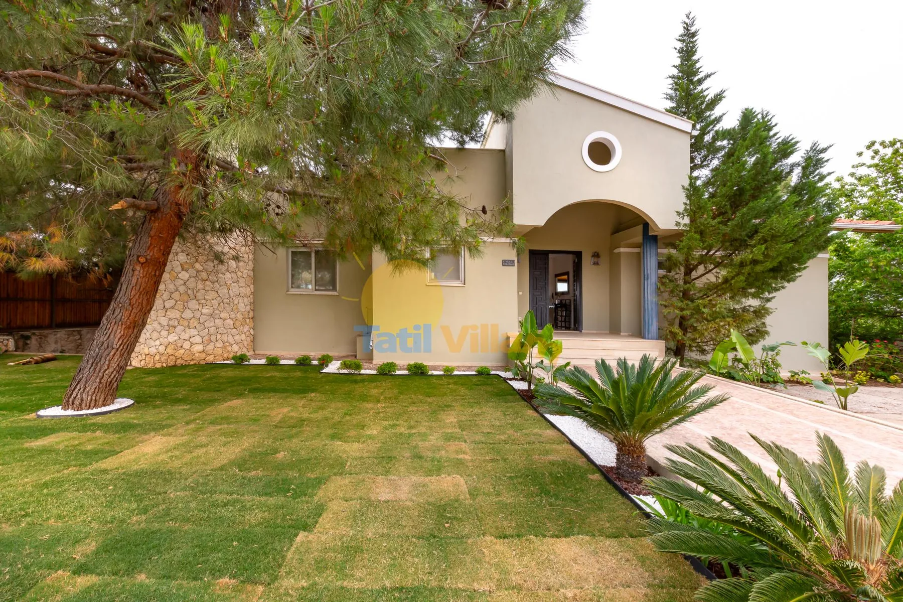 A stucco house with an arched entrance stands beside a green lawn.