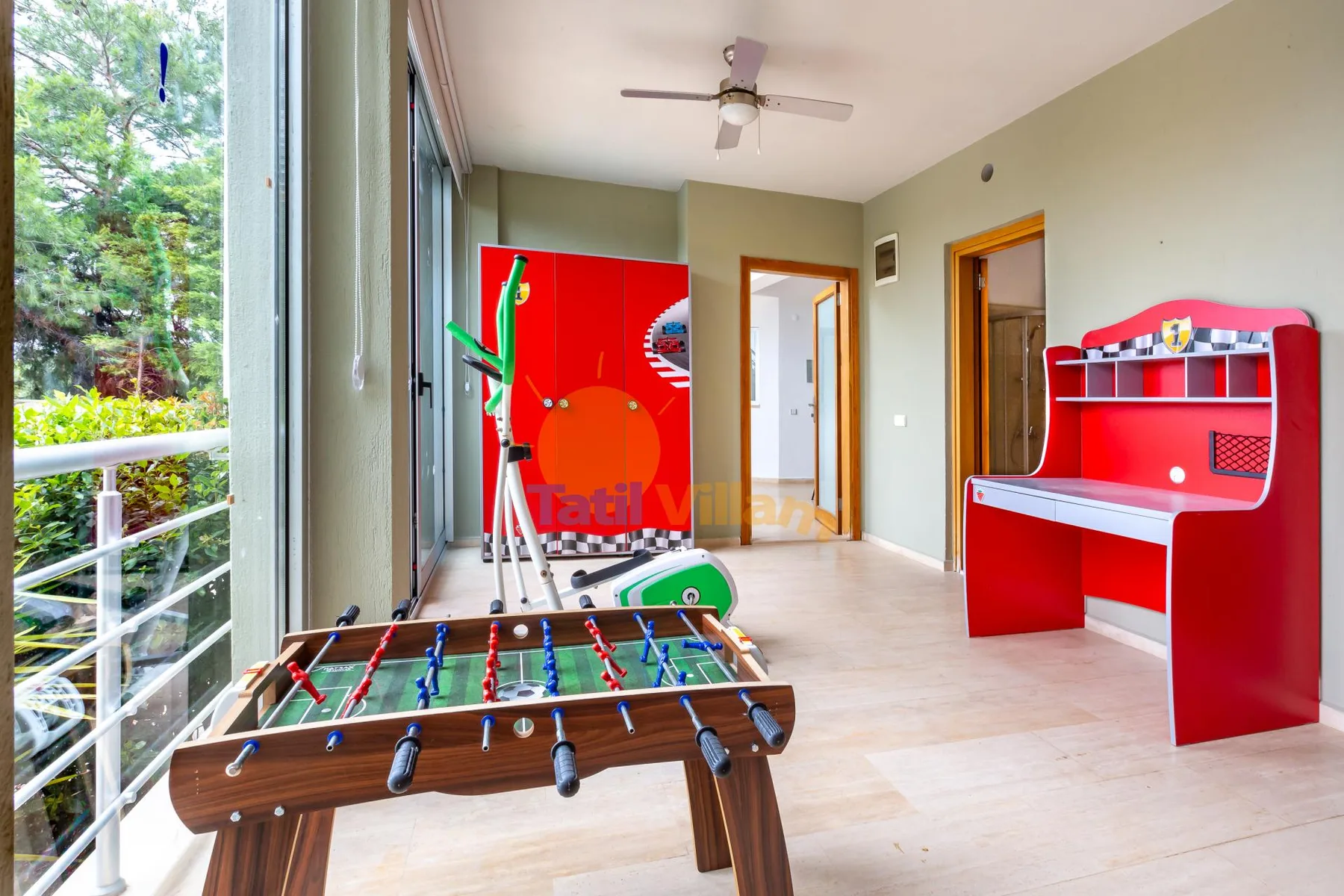 A bright game room with a foosball table, arcade machine, and red desk.