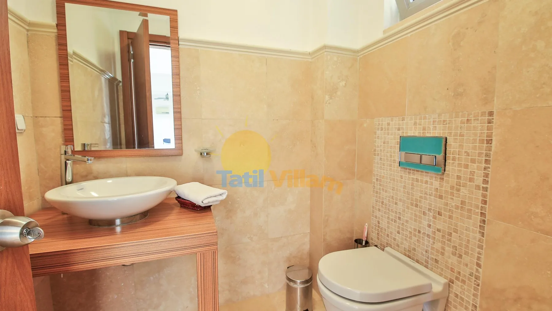A bathroom with a sink, mirror, and toilet beside a tiled wall.