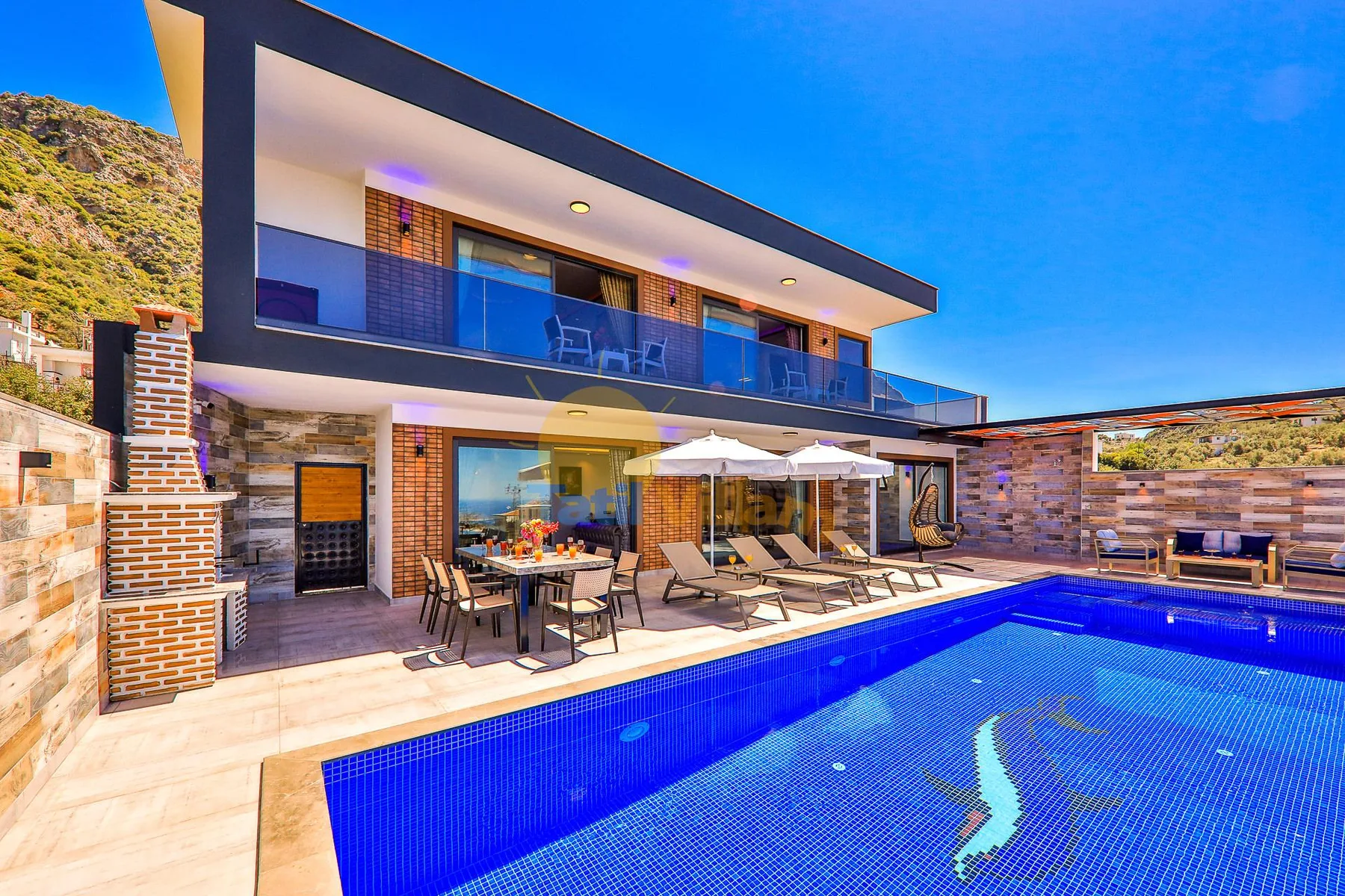 A modern house opens onto a tiled swimming pool and outdoor seating area.