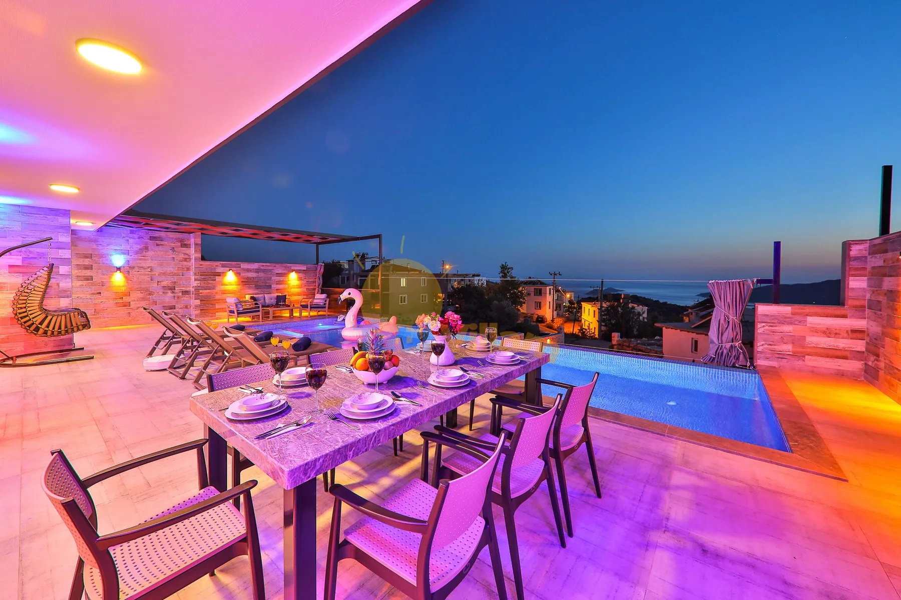 A rooftop dining area with a table beside a swimming pool at dusk.