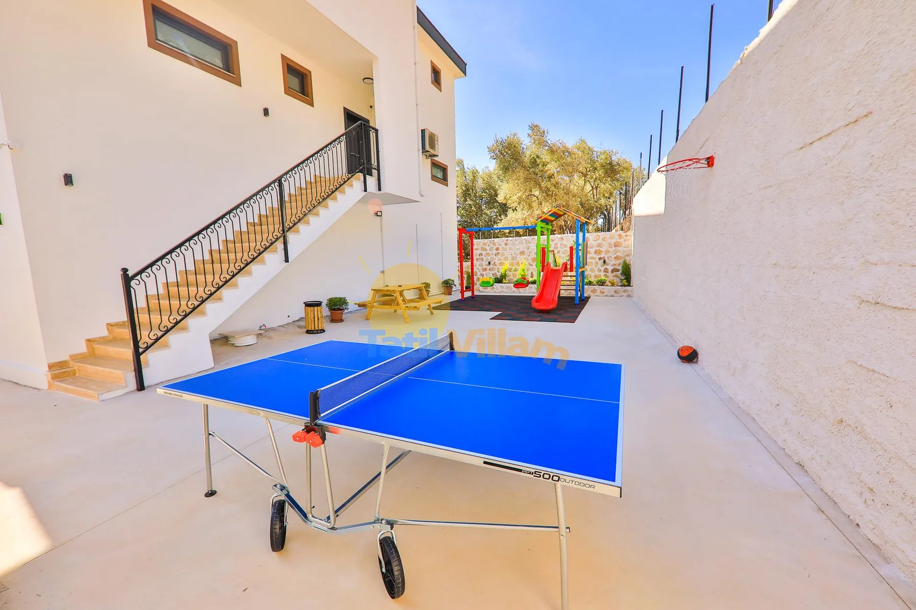 An outdoor recreation area with a blue table tennis table and a small play structure.