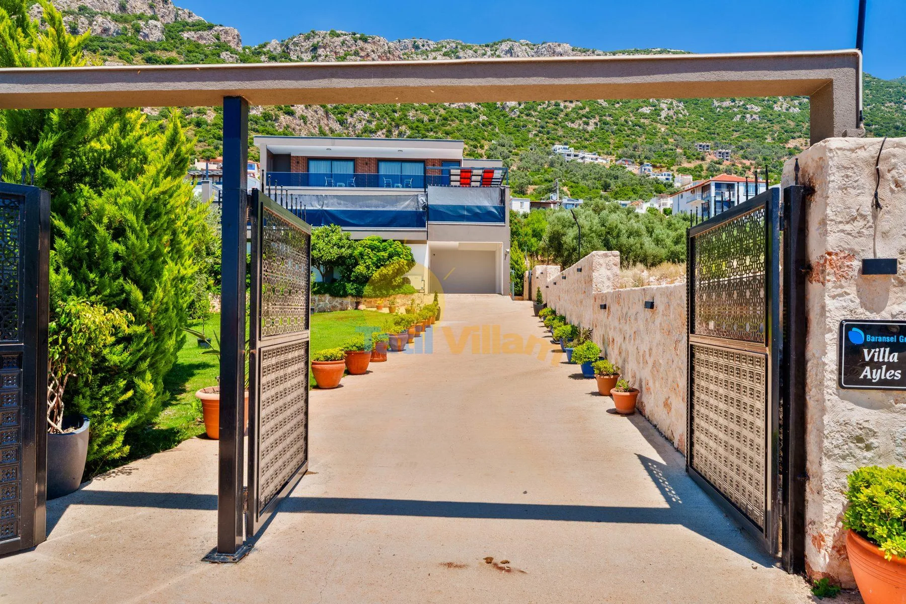 An open entrance gate frames a paved driveway leading toward a house.