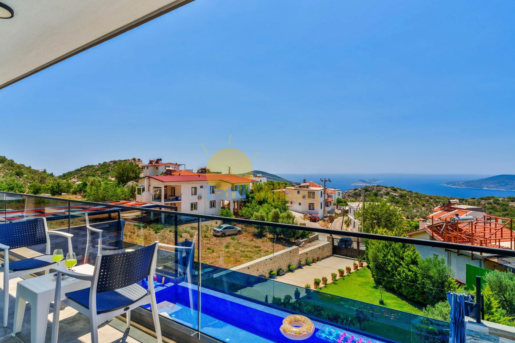 A balcony overlooks a swimming pool, hillside homes, and the sea.