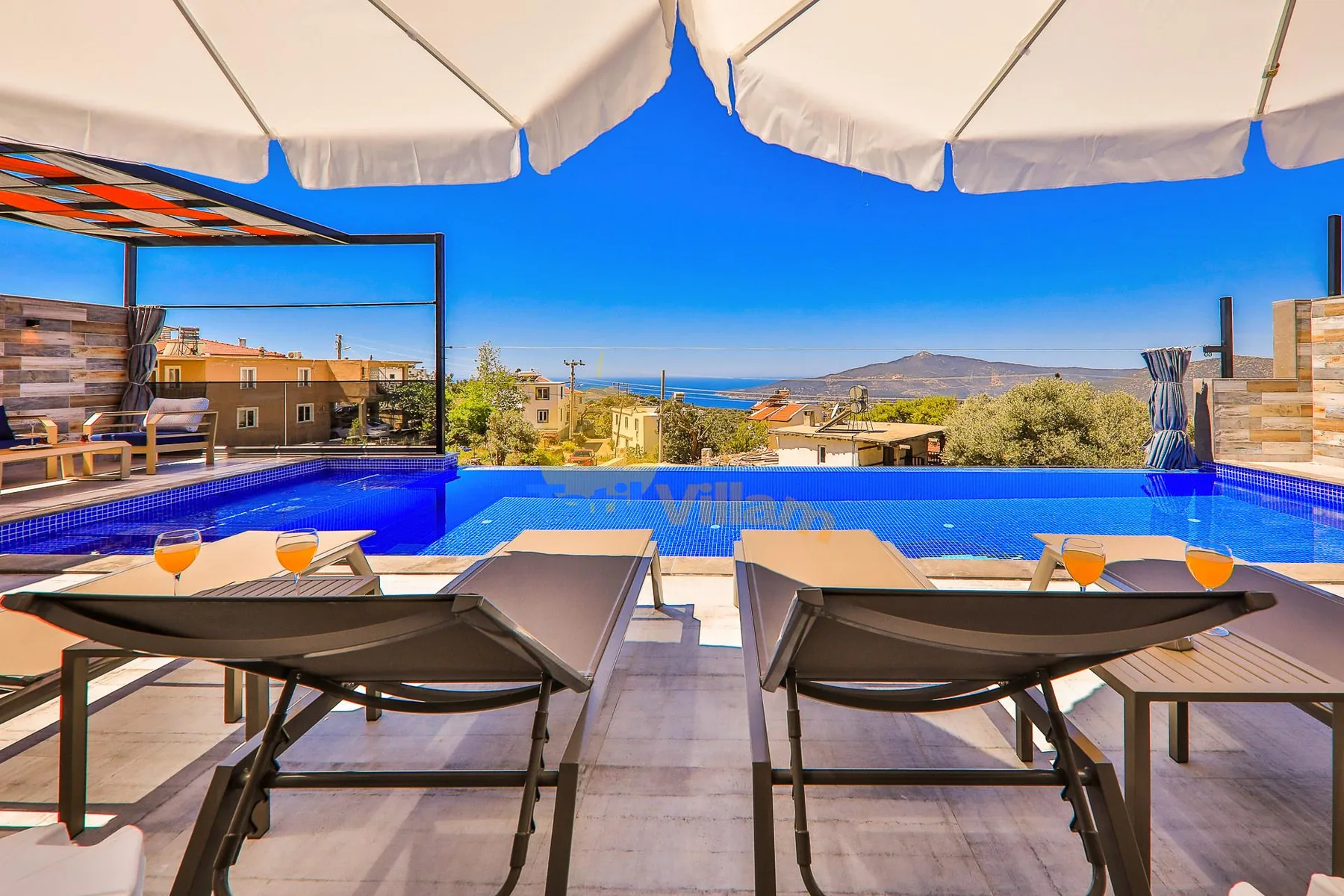 A poolside patio with lounge seating overlooks the surrounding hills and sea.