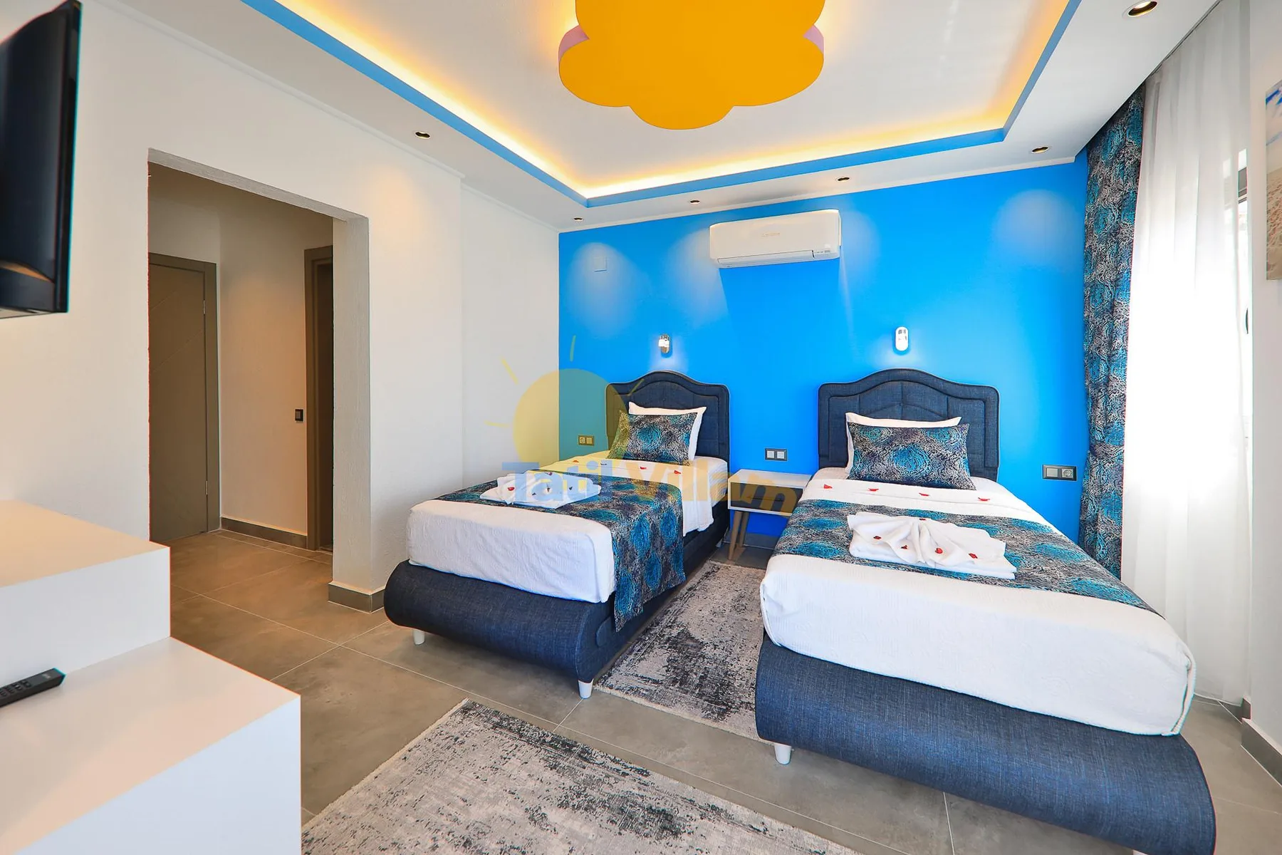 A bright bedroom with two beds against a vivid blue wall.
