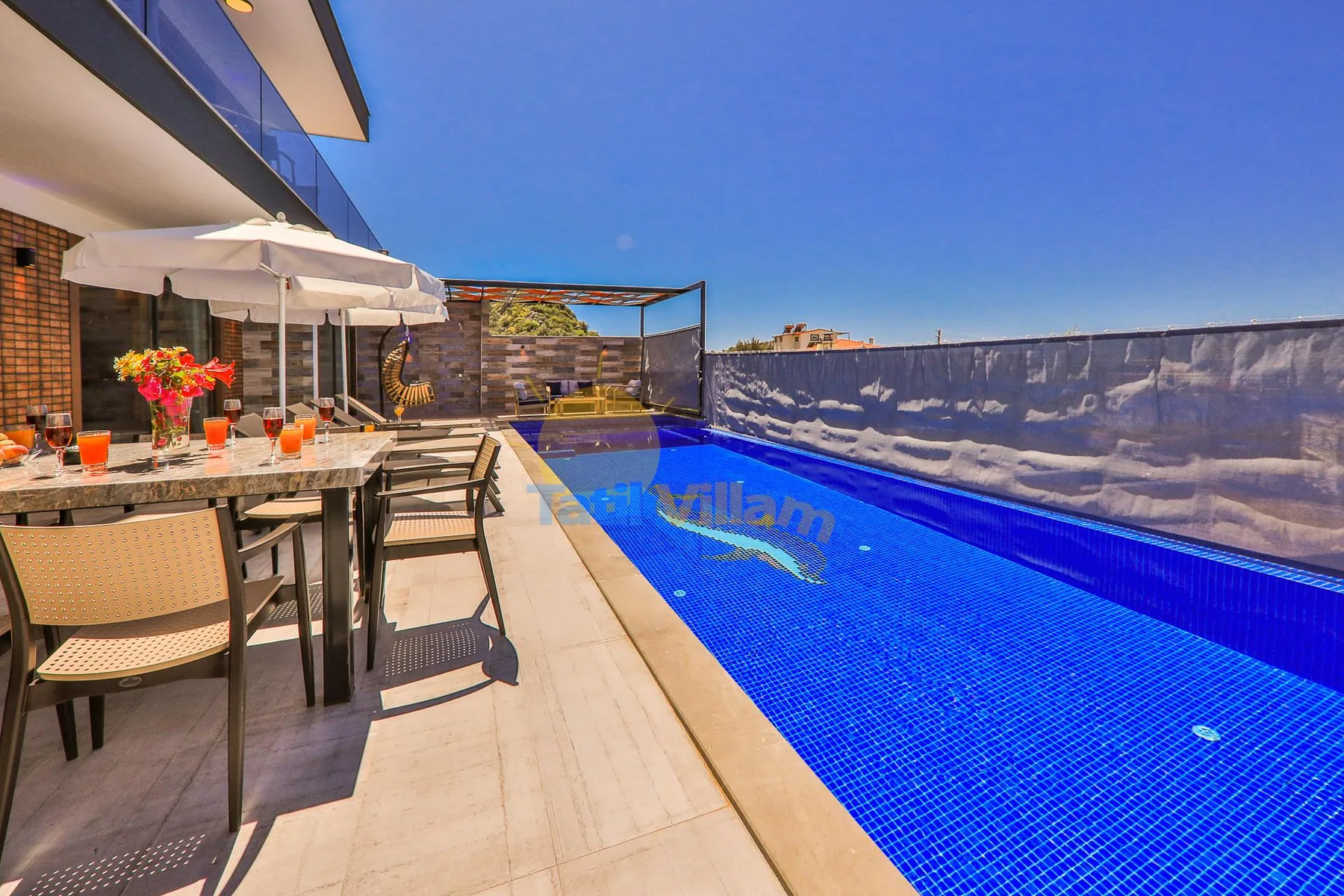 A rooftop pool beside an outdoor dining area under a clear blue sky.