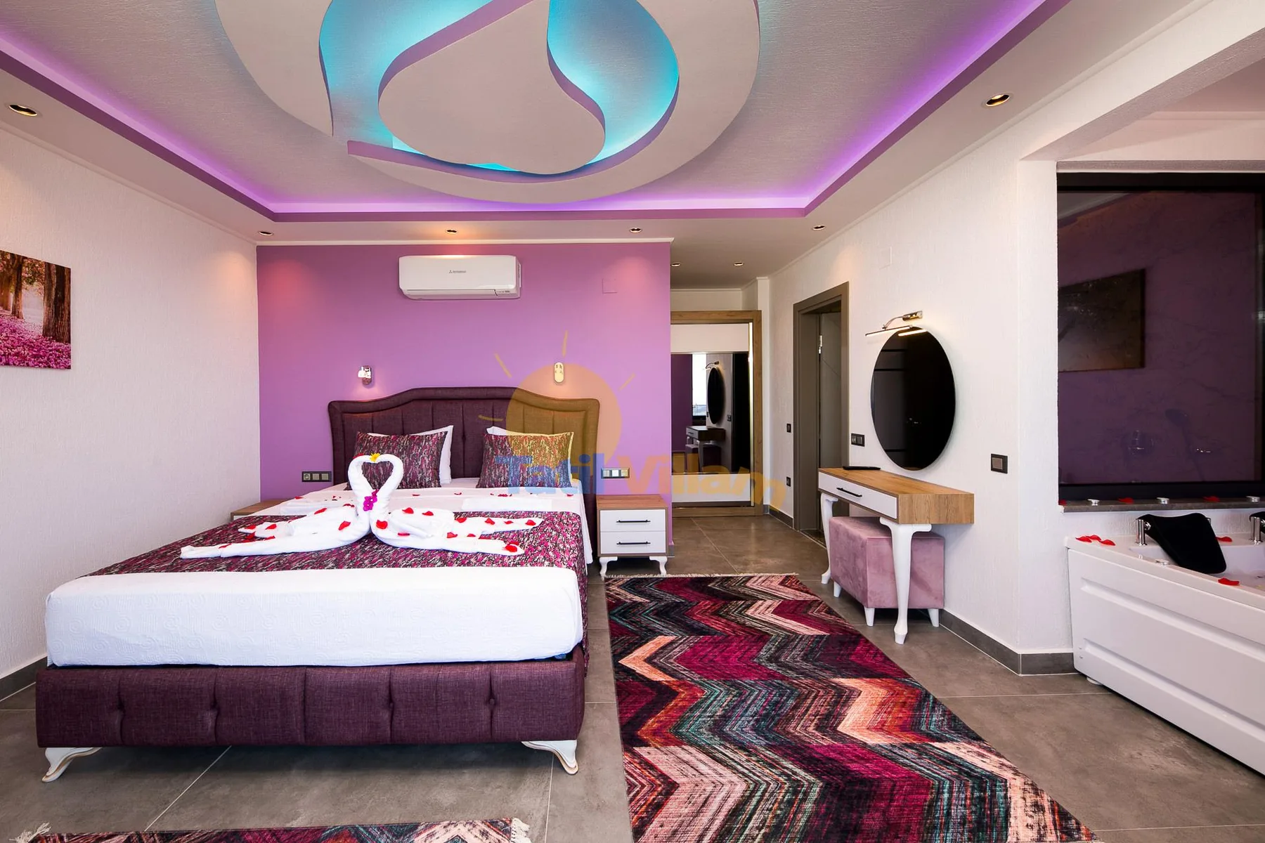 A bedroom with a large bed, colorful rug, and vanity.
