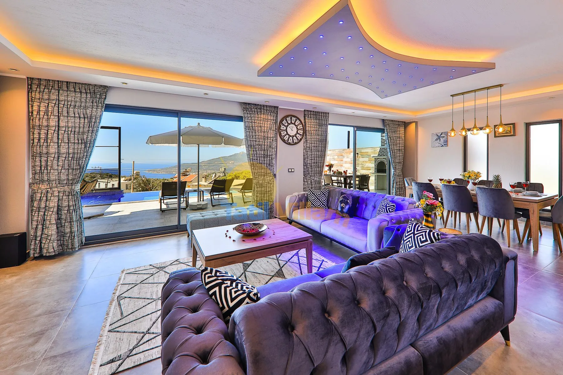 Living room with seating and a dining area beside large windows overlooking the sea.