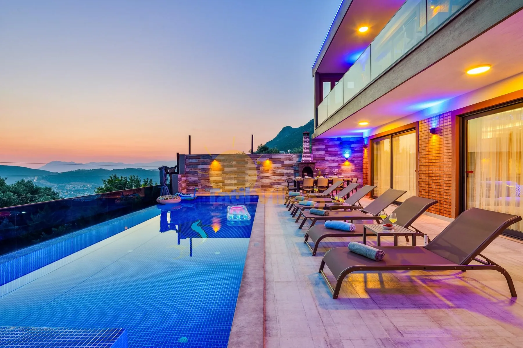 An outdoor pool beside a modern building, with loungers along the deck at sunset.