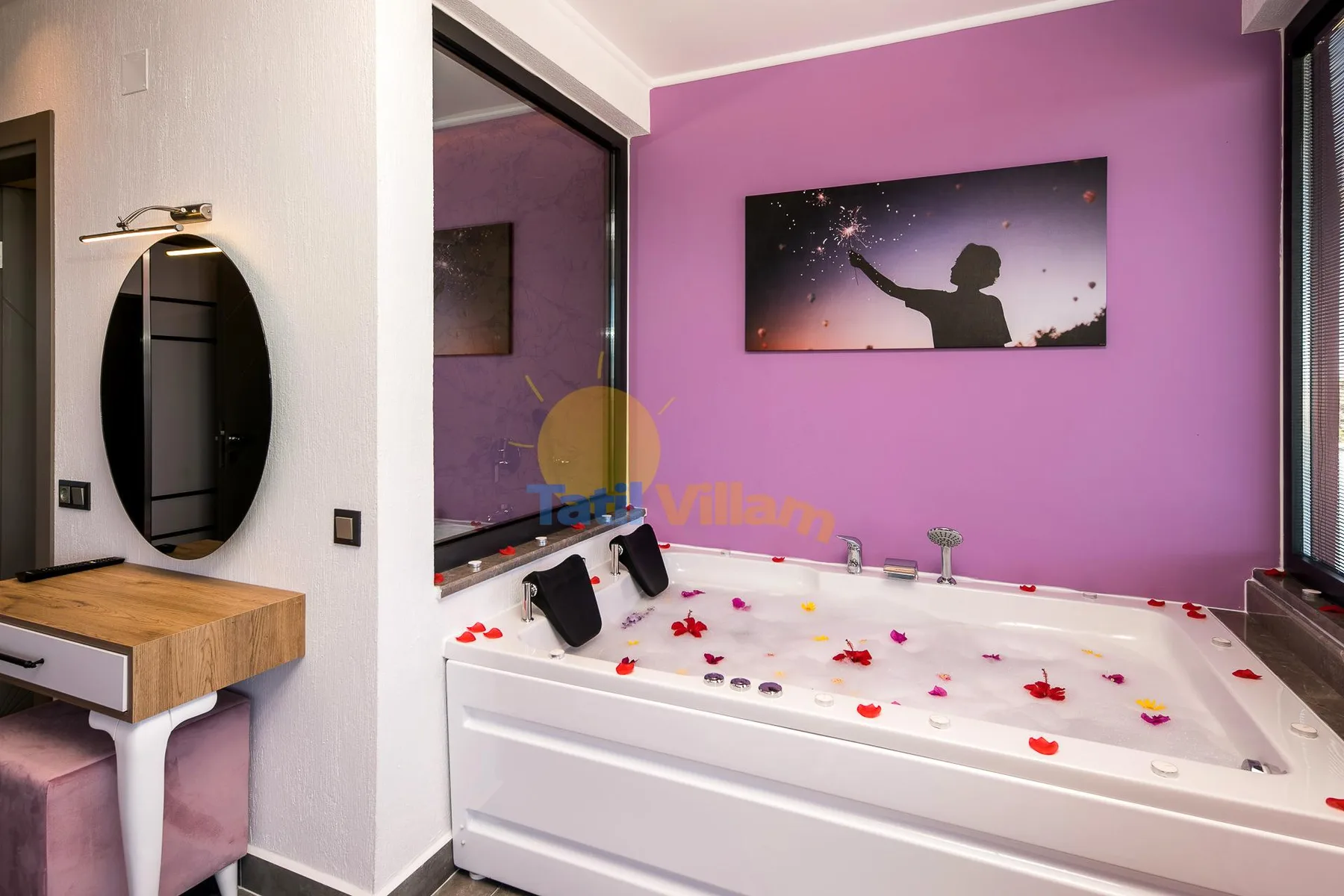A bathtub sits against a bright purple wall beneath a framed picture.