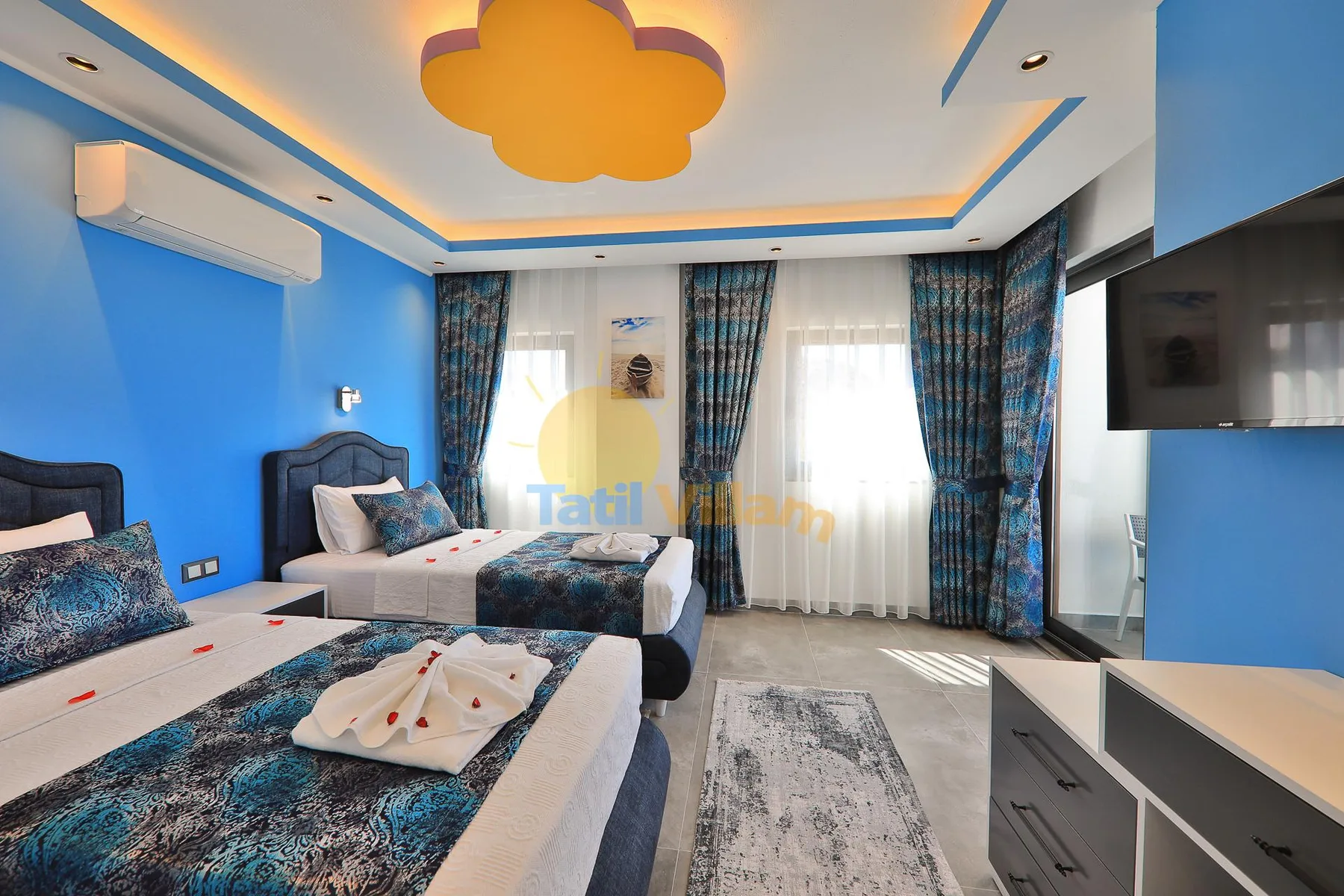 A bright bedroom with two beds, blue walls, and patterned curtains.