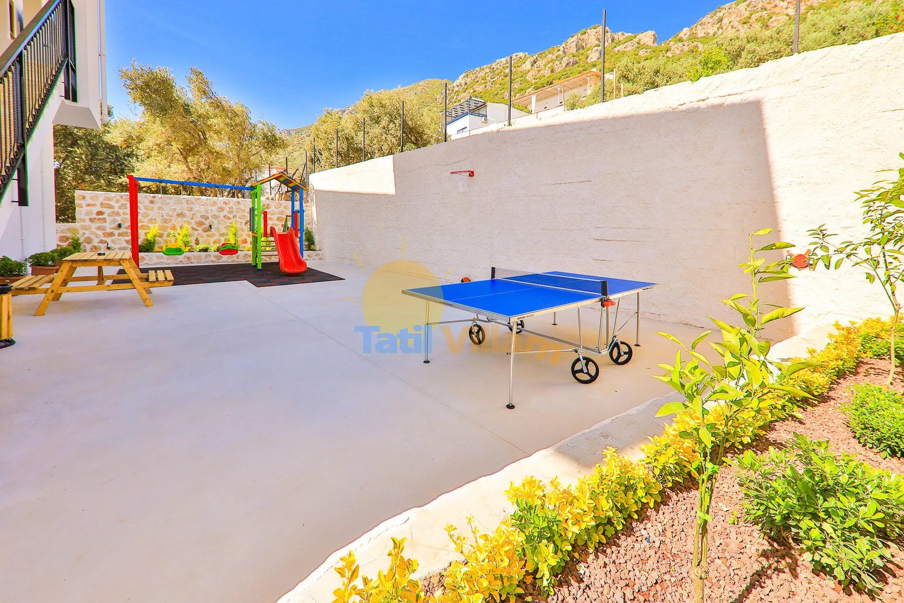 An outdoor recreation area with a blue table tennis table and a small play structure.