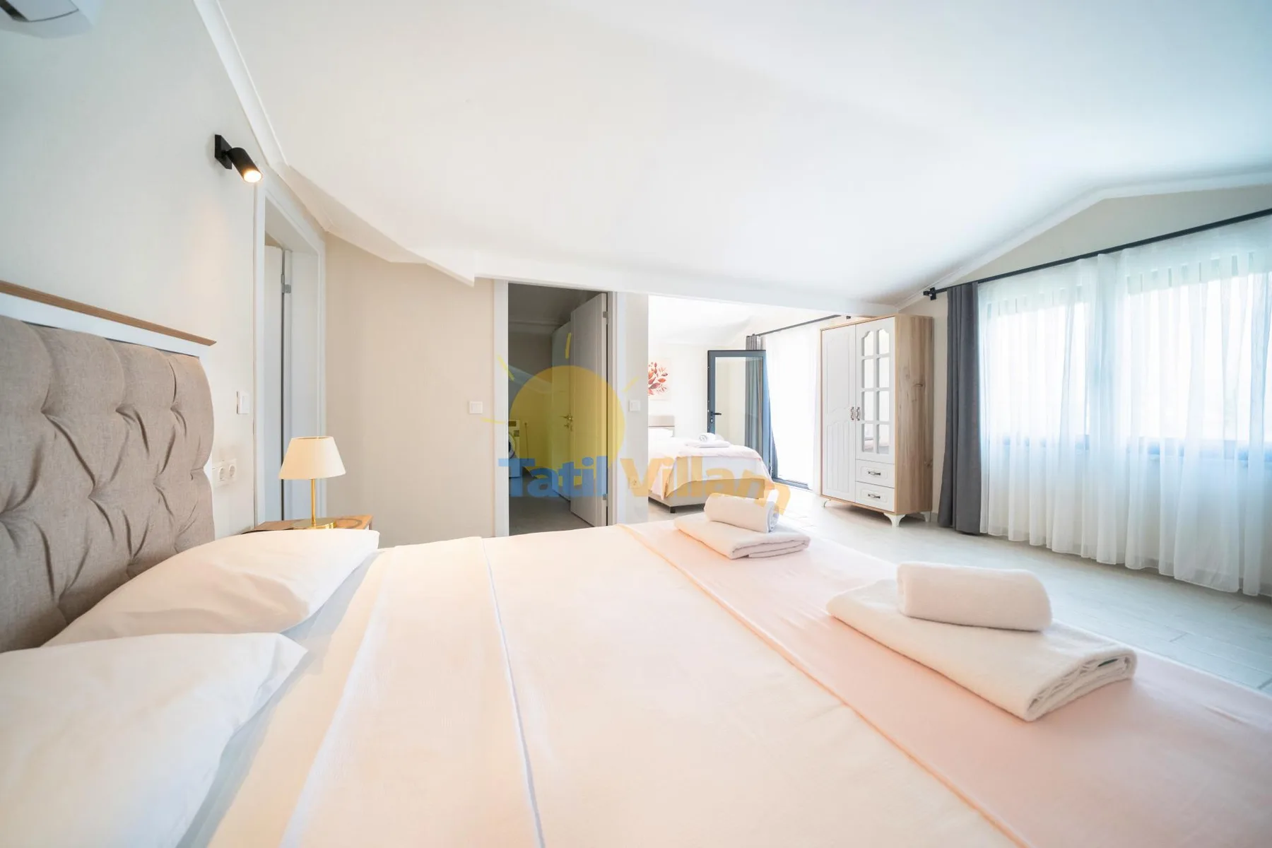 Un dormitorio luminoso con una cama grande, otra zona para dormir y cortinas translúcidas.
