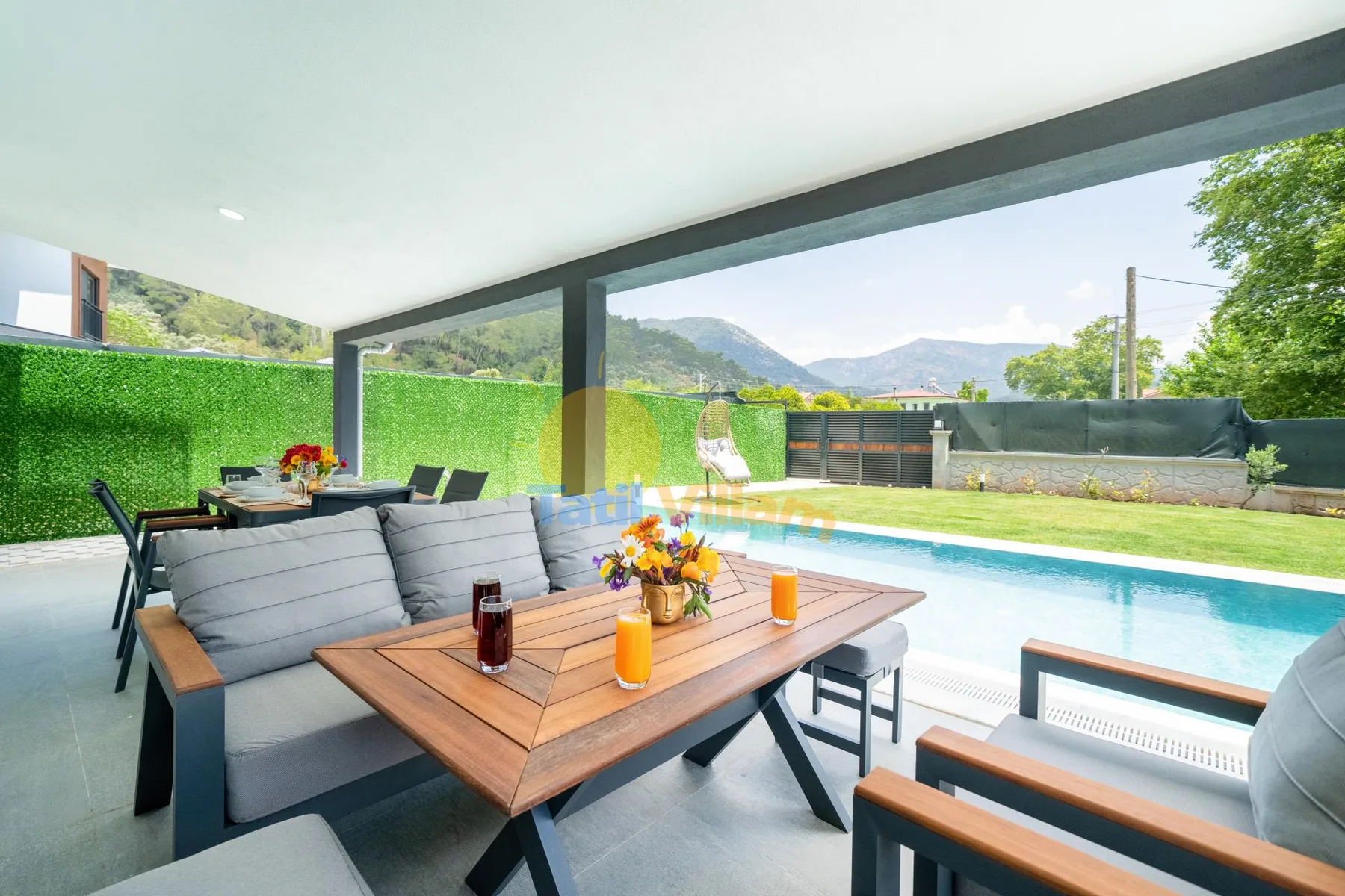 Un patio cubierto con asientos al aire libre y una piscina junto a un seto verde.