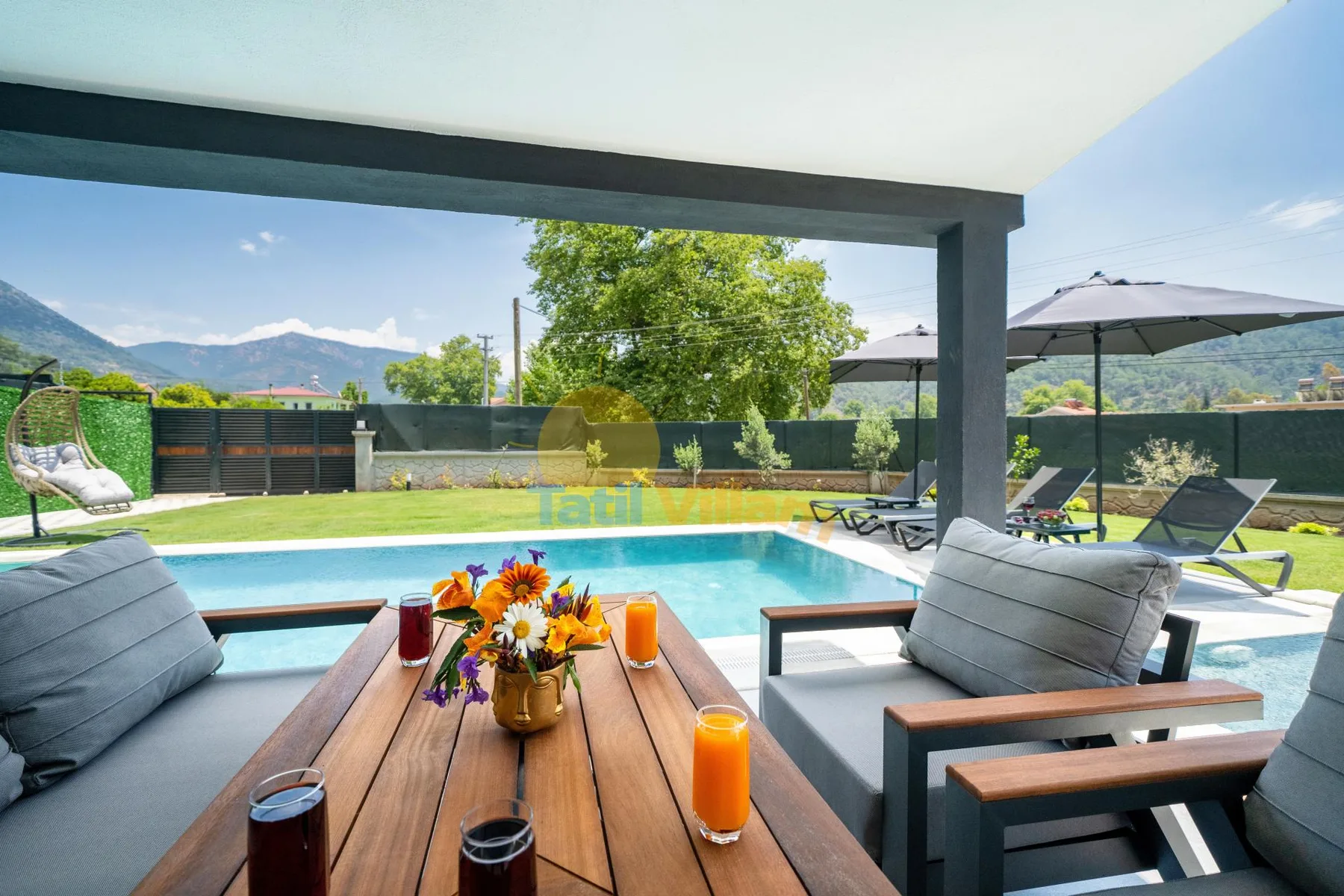 Un patio cubierto con asientos da a una piscina y un paisaje montañoso.