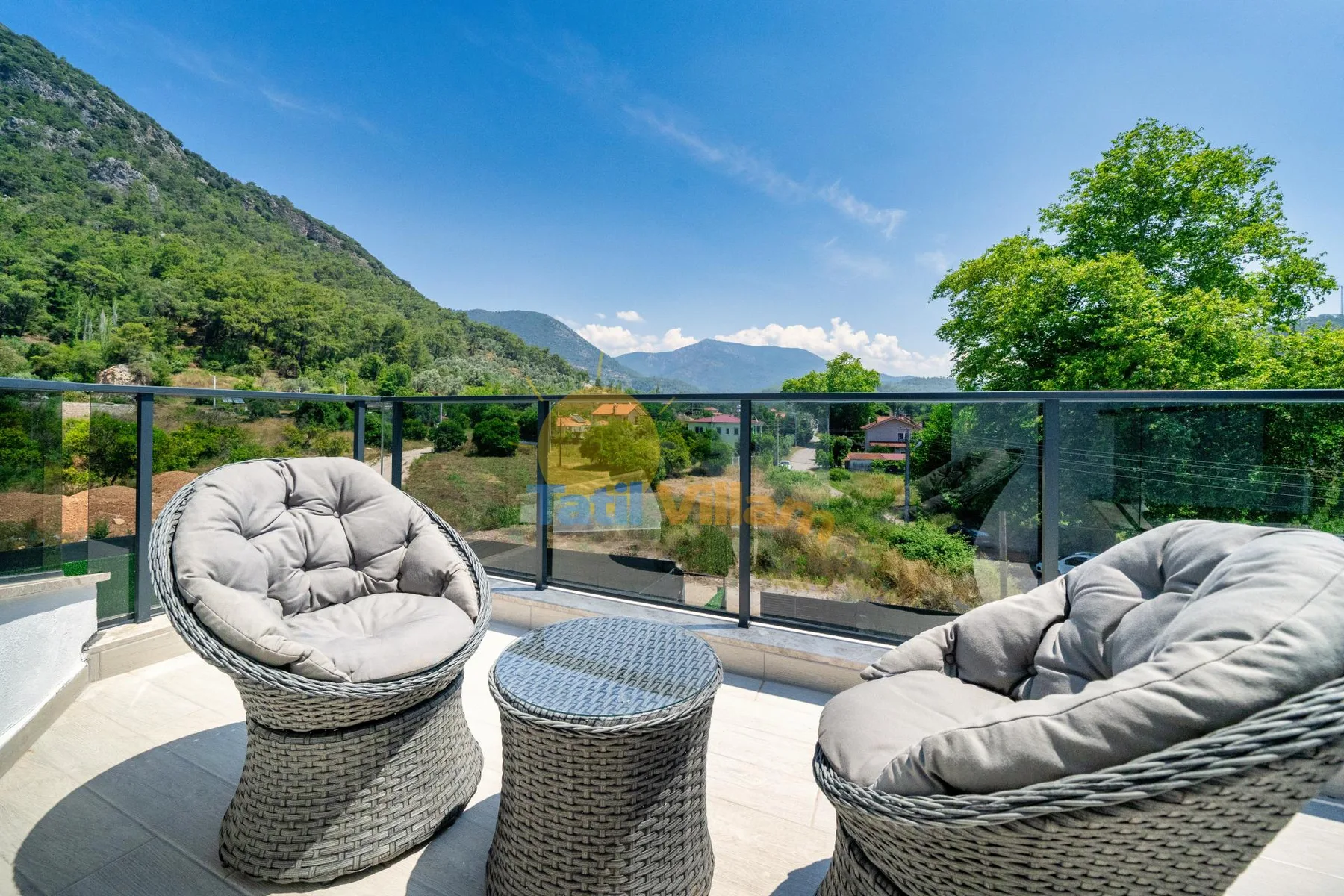 Una terraza exterior con asientos tejidos ofrece vistas a un valle verde y las colinas cercanas.