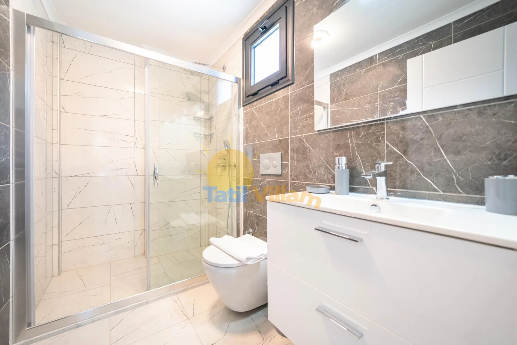 Un baño luminoso con ducha de vidrio, inodoro y tocador blanco.