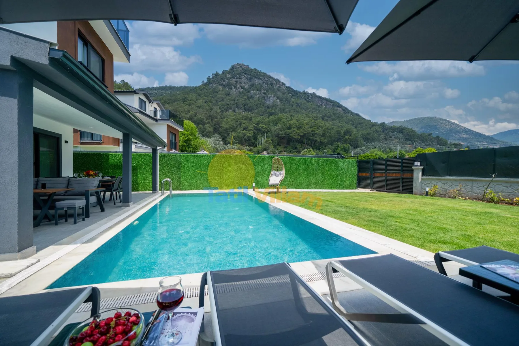 Una piscina al aire libre junto a un césped, con colinas al fondo.