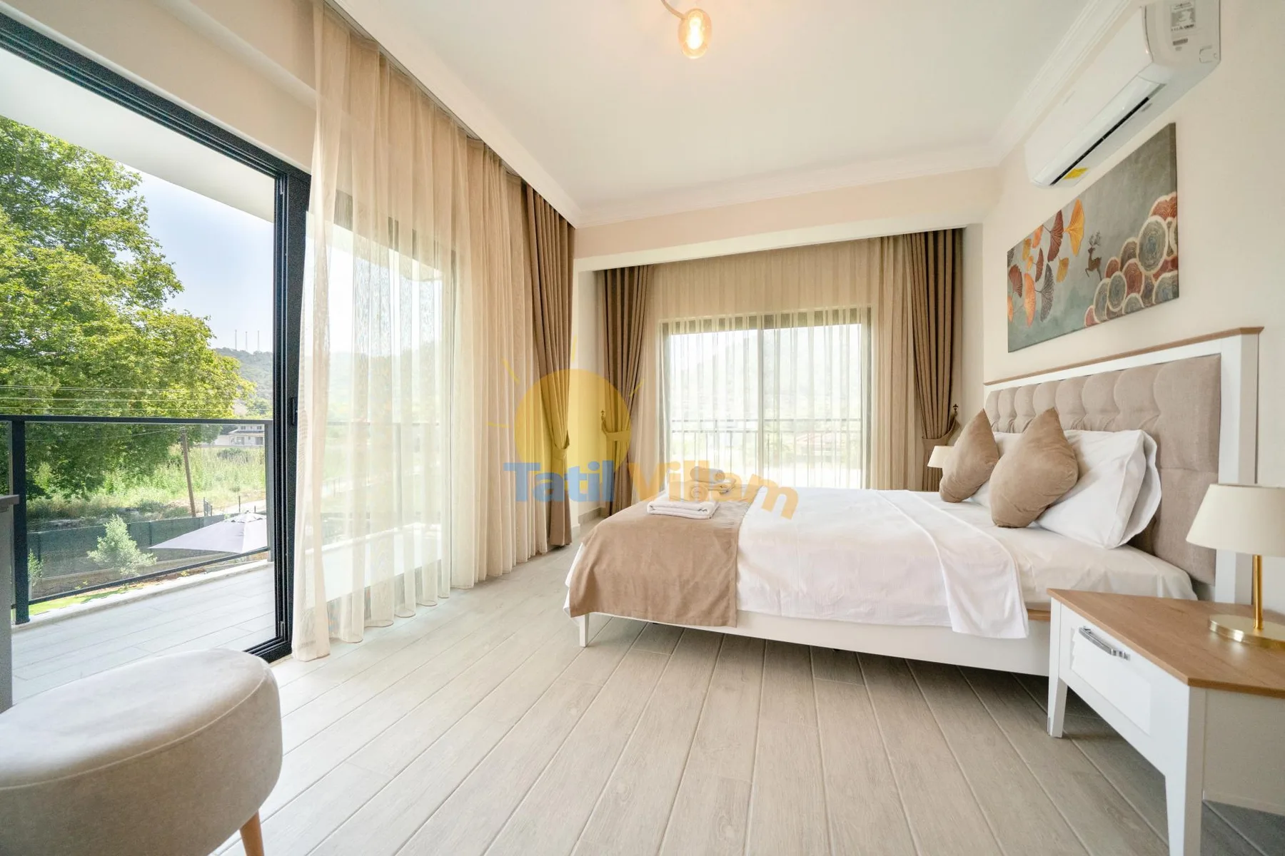 Un dormitorio luminoso con una cama junto a grandes ventanas y cortinas transparentes.