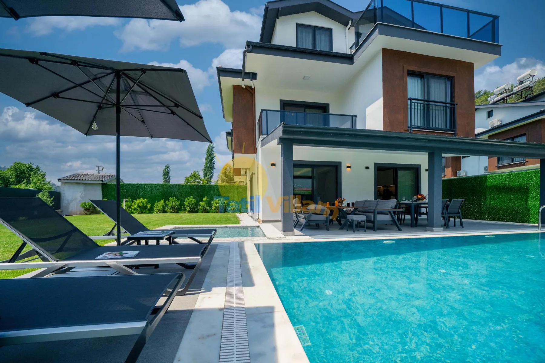 Una piscina y tumbonas junto a una casa moderna de varios pisos.