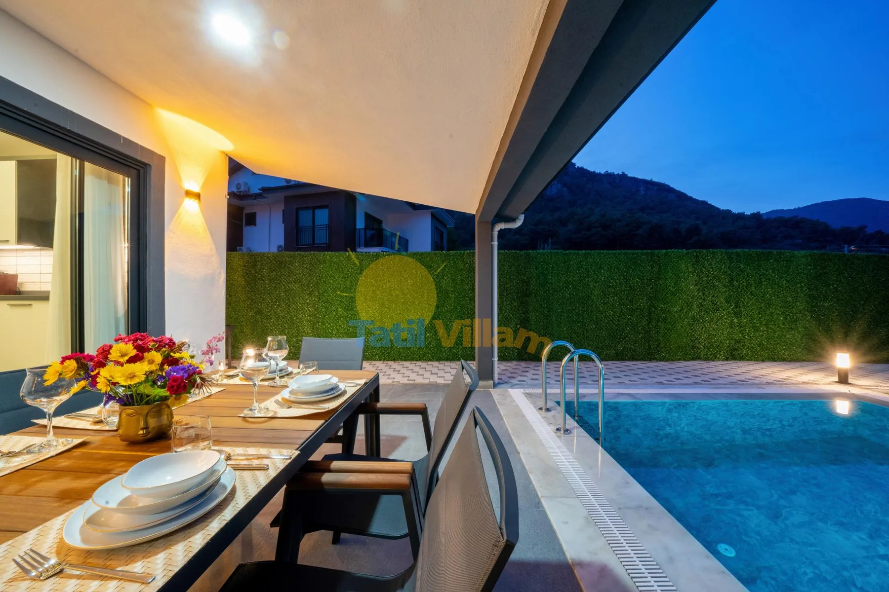 Una zona de comedor exterior cubierta junto a una piscina al anochecer.