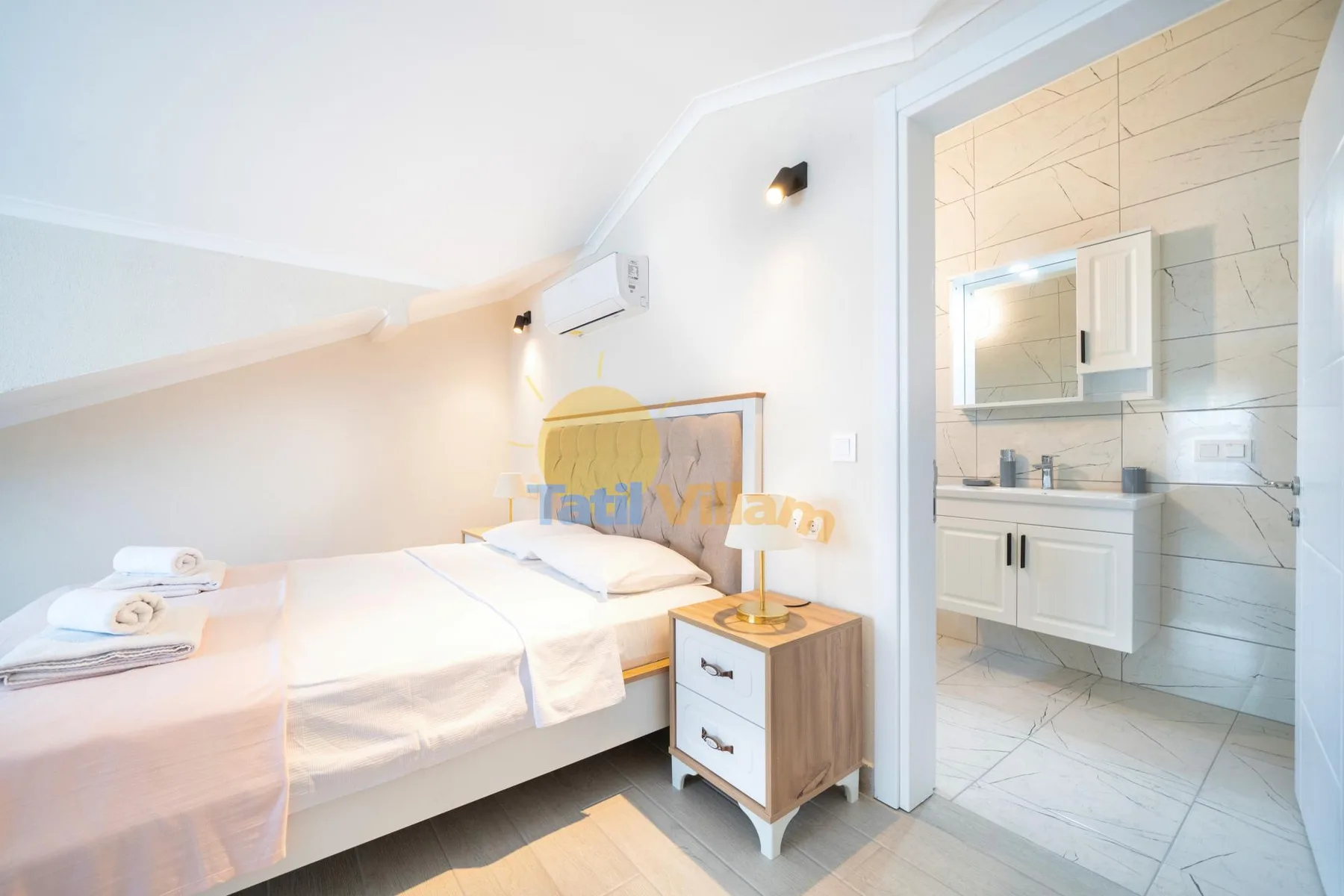 Un dormitorio luminoso con dos camas y un baño contiguo.