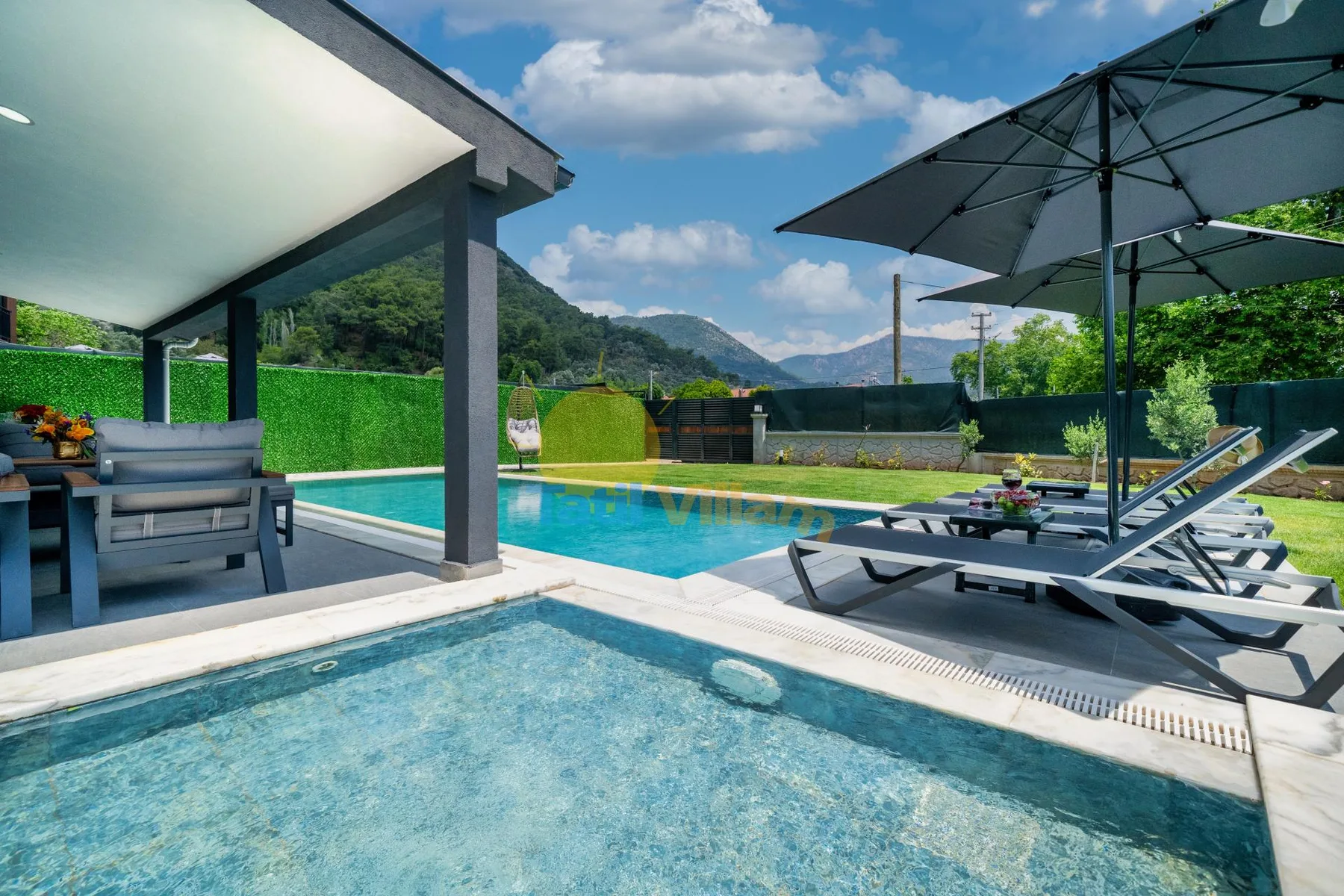 Una zona de piscina al aire libre con tumbonas y colinas verdes al fondo.