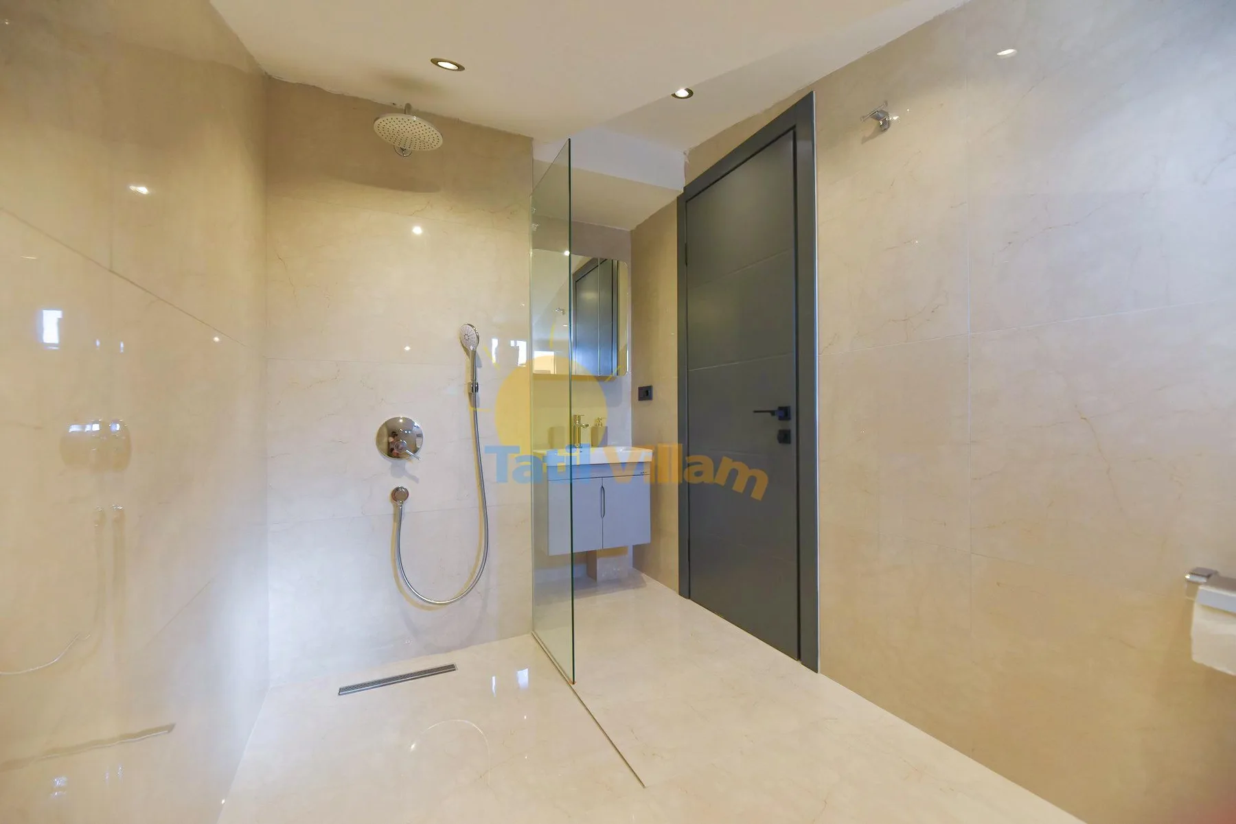 A tiled bathroom has a glass shower screen, wall-mounted shower fixtures, and a dark door.