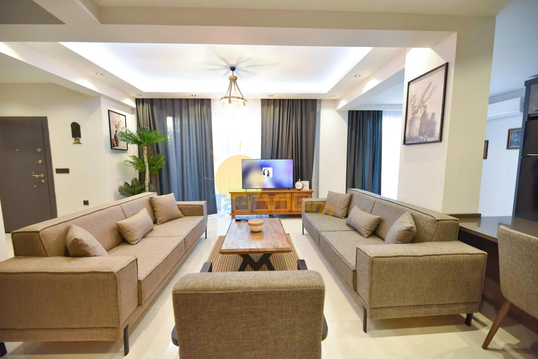 A bright living room has two beige sofas facing a television, with a wooden coffee table between them.