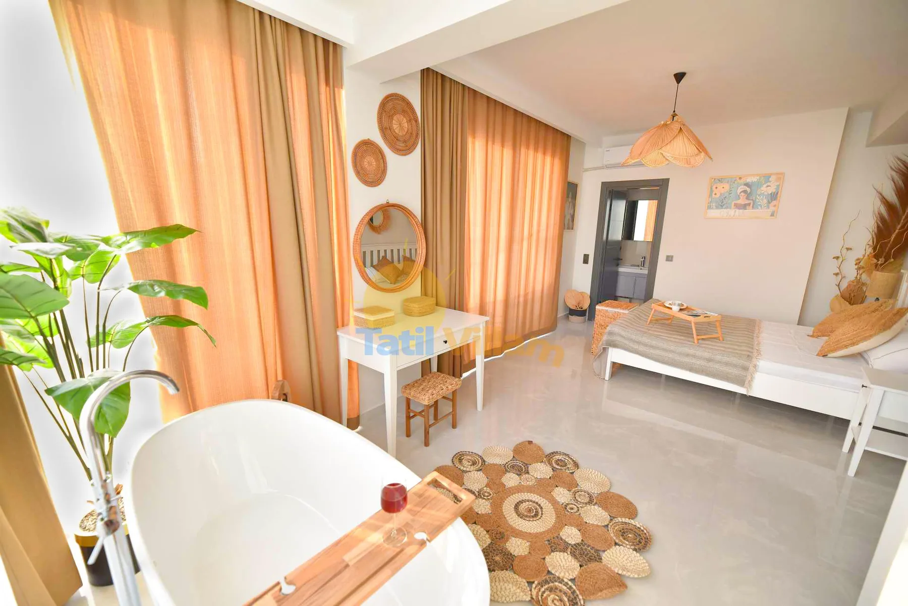 A bright bedroom has a white bed, freestanding bathtub, small vanity, and warm orange curtains.