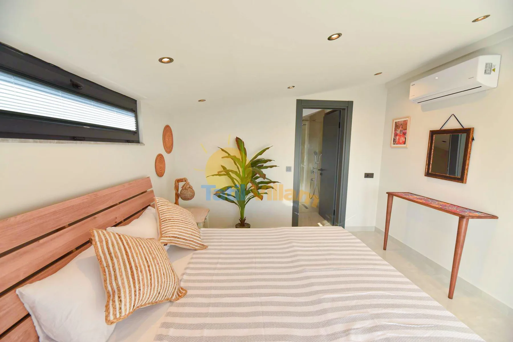A bedroom with a striped bed, wooden headboard, potted plant, and wall-mounted air conditioner.