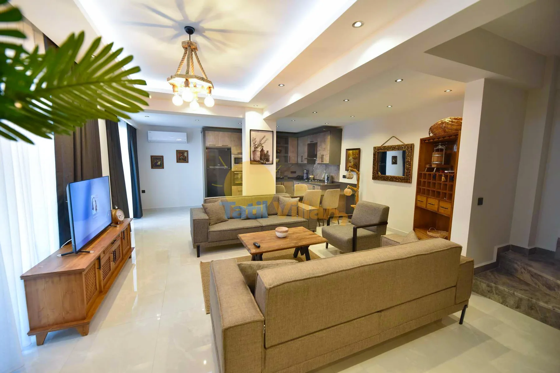 A bright living room with beige sofas, a coffee table, a television, and a dining area beyond.
