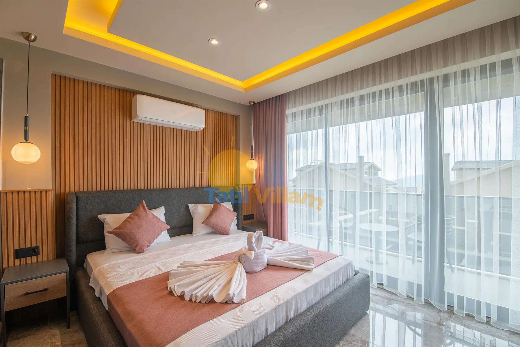 A bedroom with a double bed, wood-slat wall, pendant lights, and floor-to-ceiling curtained windows.