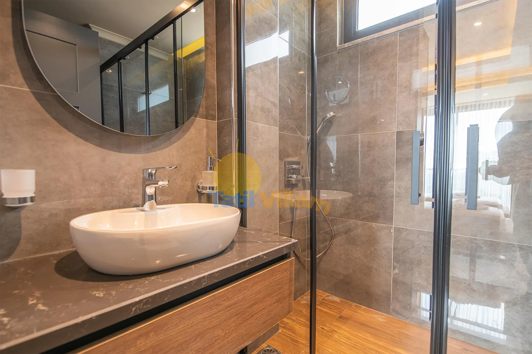 A modern bathroom with a white vessel sink, round mirror, and glass-enclosed shower.