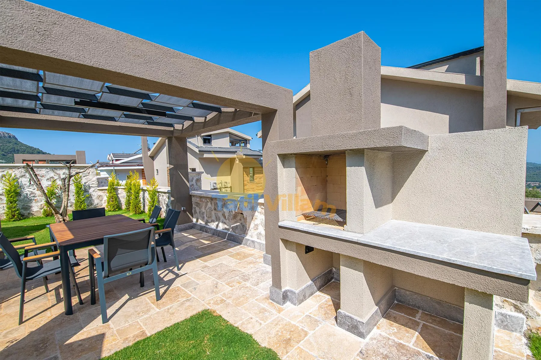 A sunlit outdoor patio has a pergola, a dining table with chairs, and a built-in barbecue.