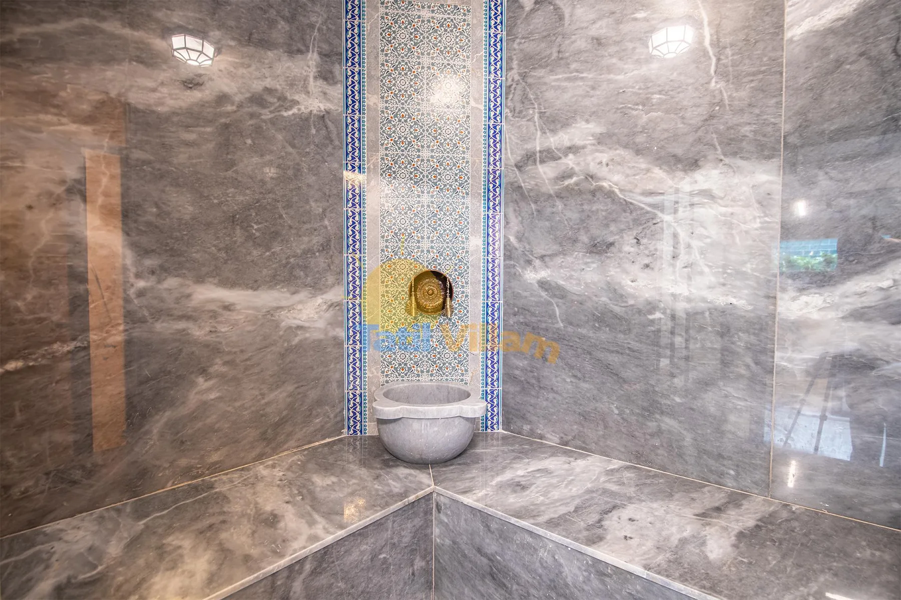 A marble-lined bathroom corner features a small wall-mounted basin beneath a decorative mosaic panel.