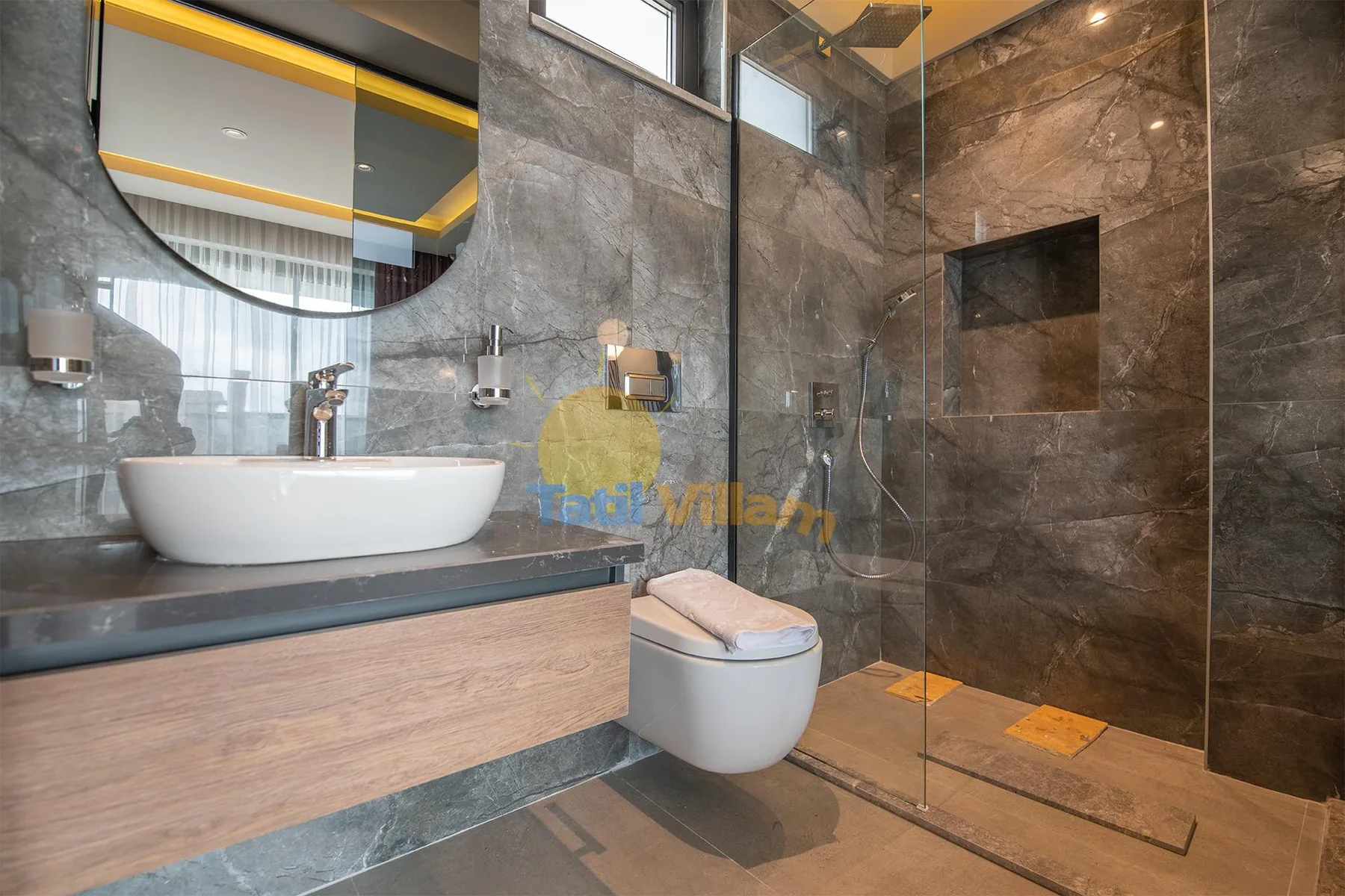 A modern bathroom features a vessel sink, wall-mounted toilet, and glass-enclosed shower with stone-look tile.