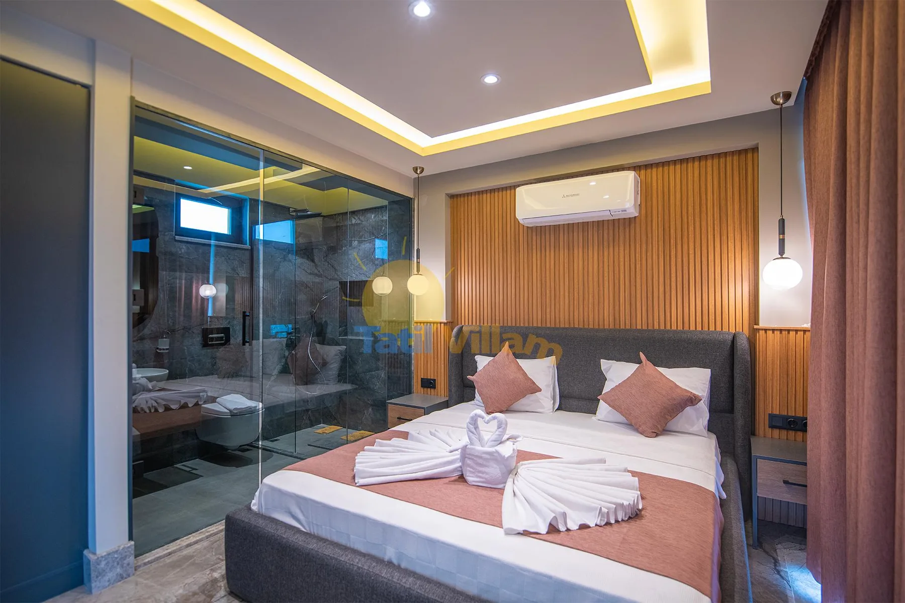 A bedroom with a double bed, folded towels, a wall-mounted air conditioner, and glass partitions.