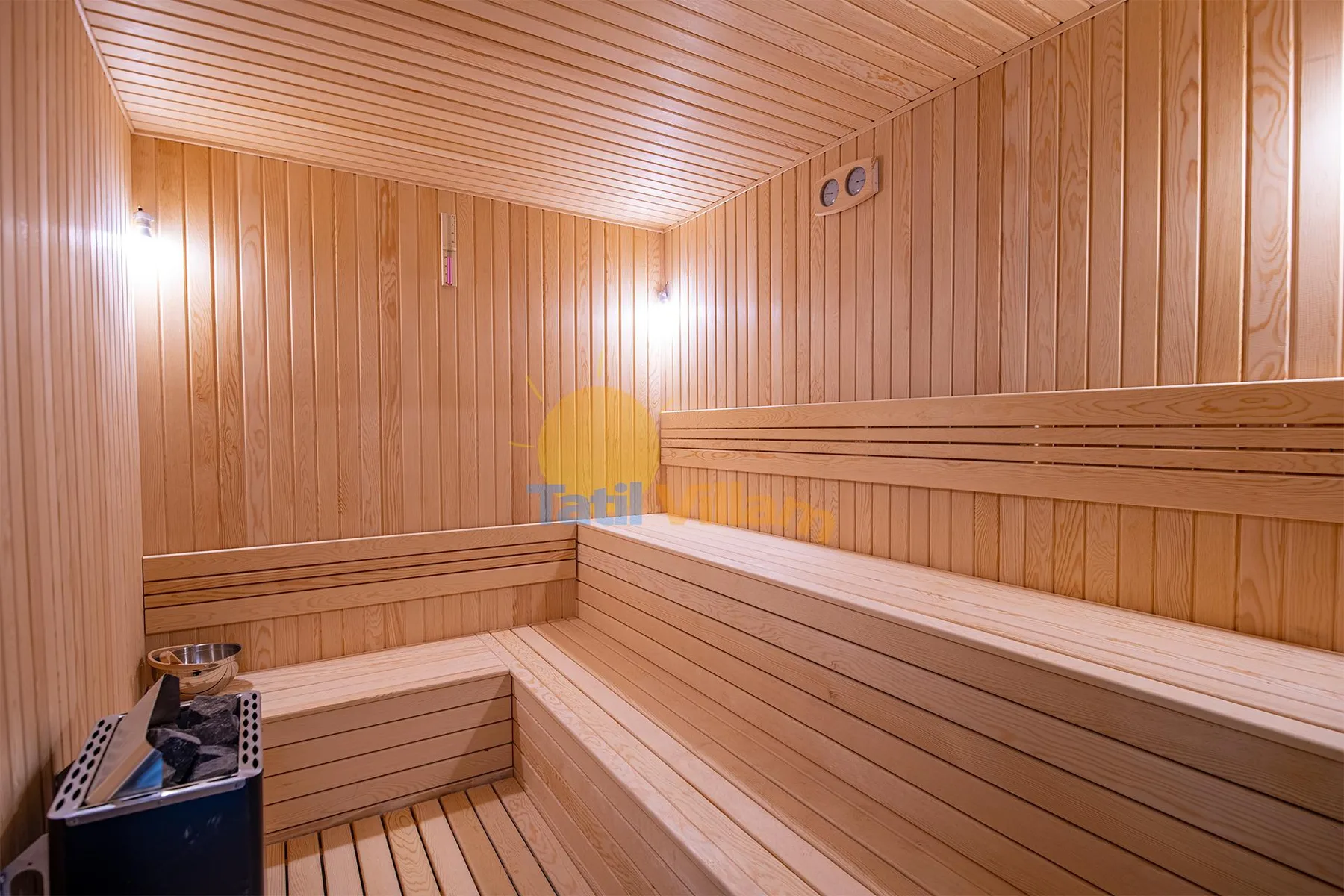 A wood-paneled sauna has tiered wooden benches, a slatted ceiling, and a heater in the corner.