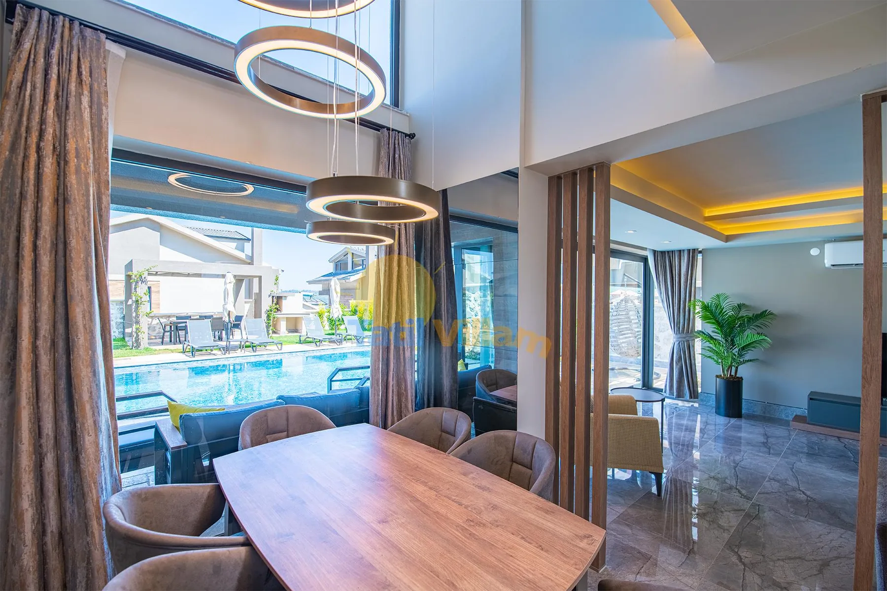A dining table and chairs sit beside floor-to-ceiling windows overlooking a swimming pool.