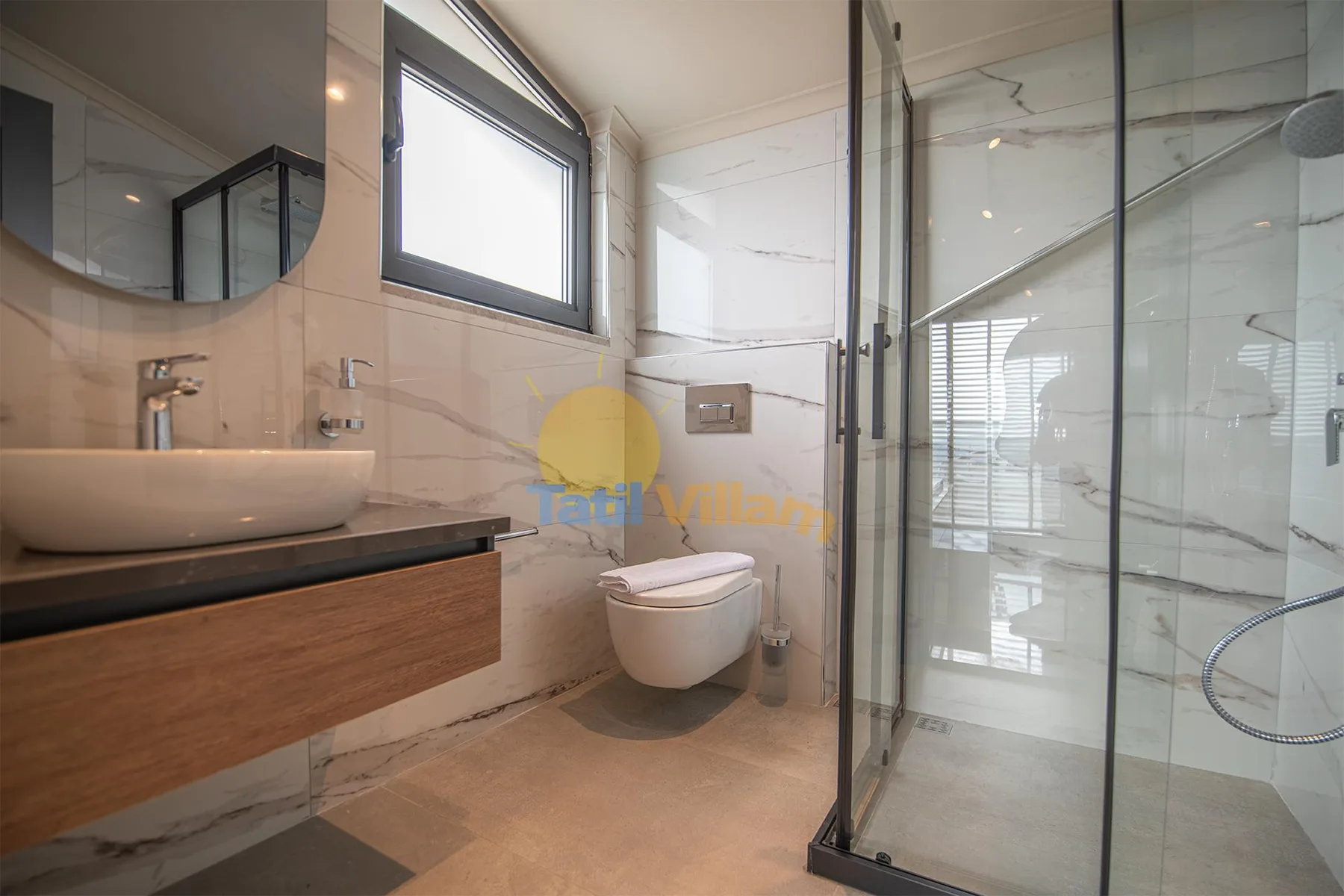 A modern bathroom with a wall-mounted toilet, wood-front vanity, and glass-enclosed shower.