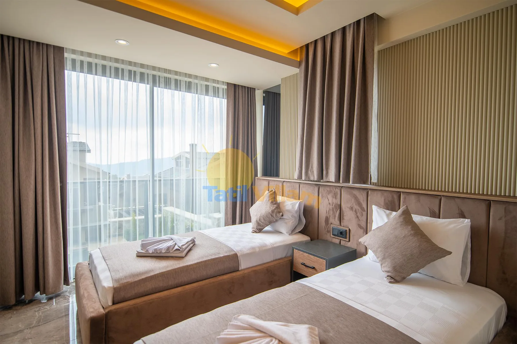 A bedroom with two beds, a bedside table, and floor-to-ceiling curtains over a glass balcony door.