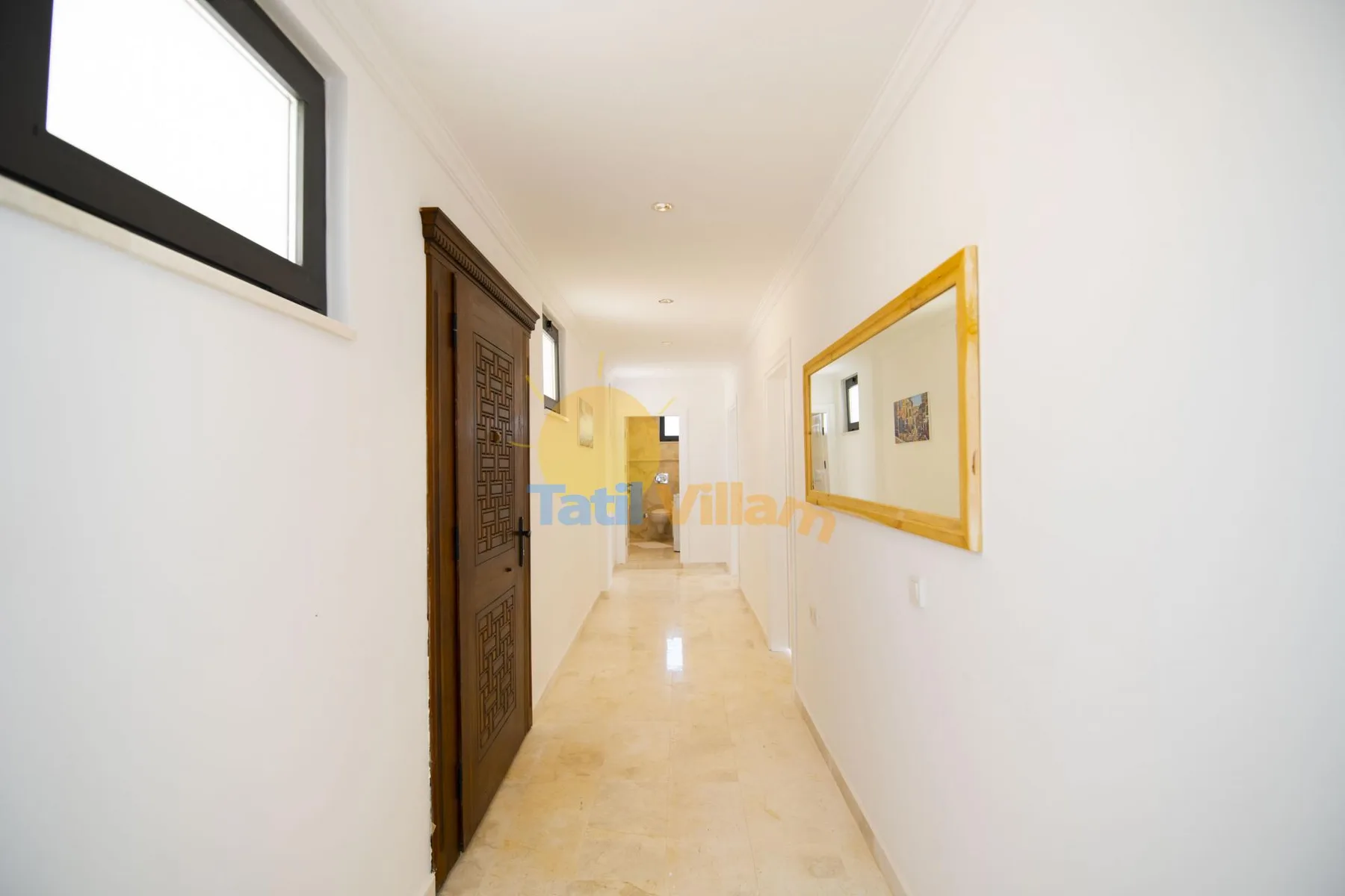 A bright hallway with a framed mirror and a dark wooden door.