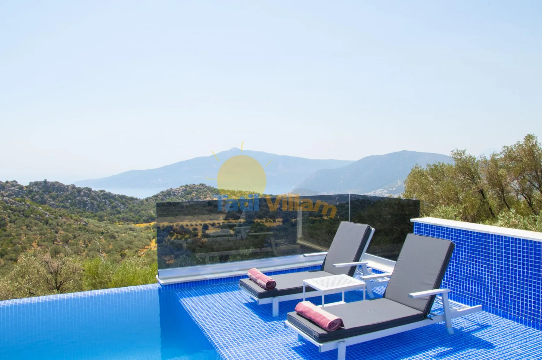 A rooftop pool overlooks wooded hills, with loungers beside the water.